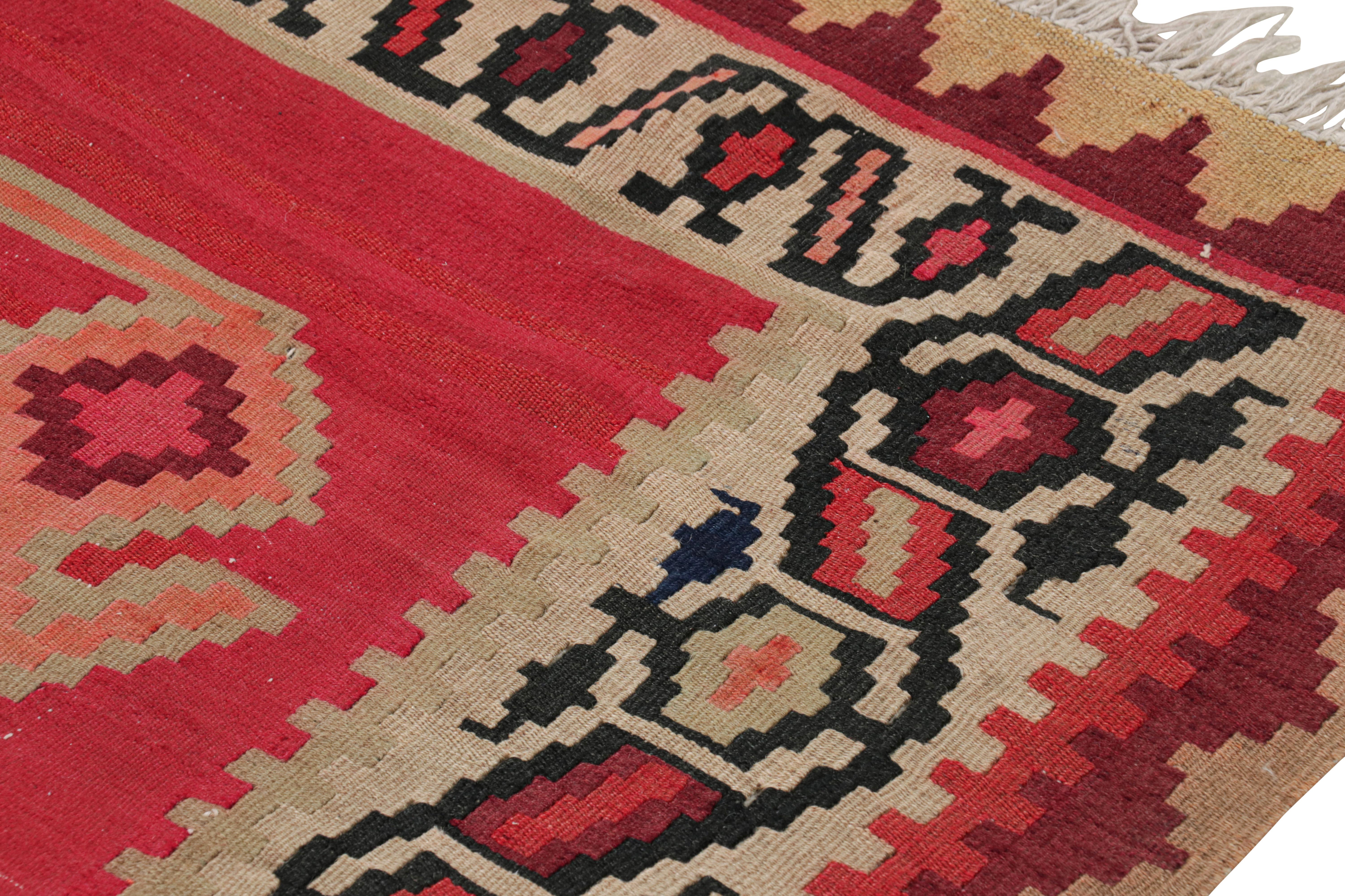 Dieser um 1950-1960 aus flach gewebter Wolle handgefertigte Vintage-Teppich ist ein persischer Kilim aus der Mitte des Jahrhunderts in einem auffallend warmen Rot, das durch ein marineblaues und orangefarbenes Medaillon-Feldmuster und versöhnliche