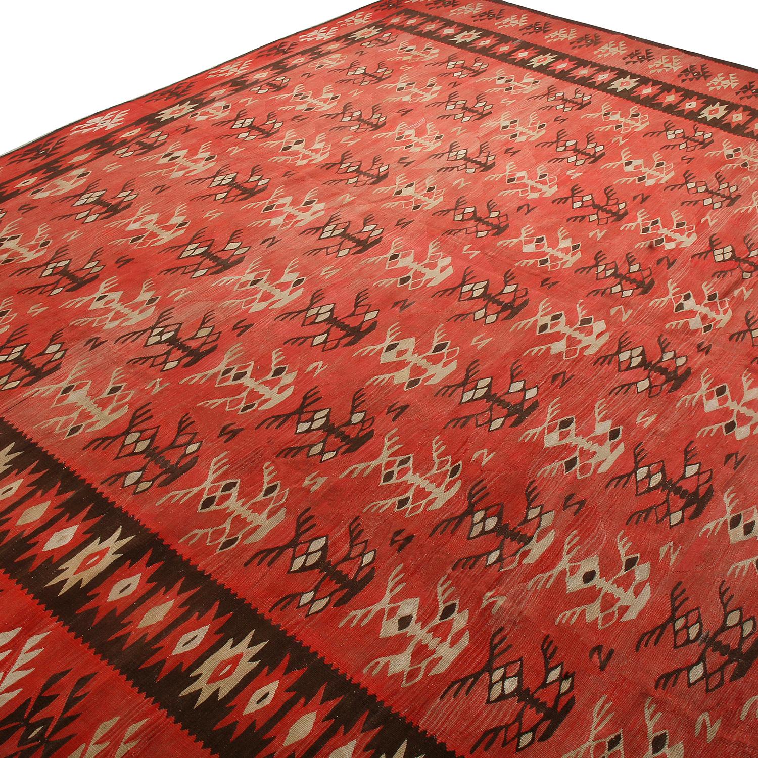 Handwoven in Turkey originating between 1950-1960, this vintage mid-century wool Kilim hails from the Pirot, also known as Sarkoy (Sarköy). The Classic salmon-red colorway plays well off this unique variation of the black border and beige-brown