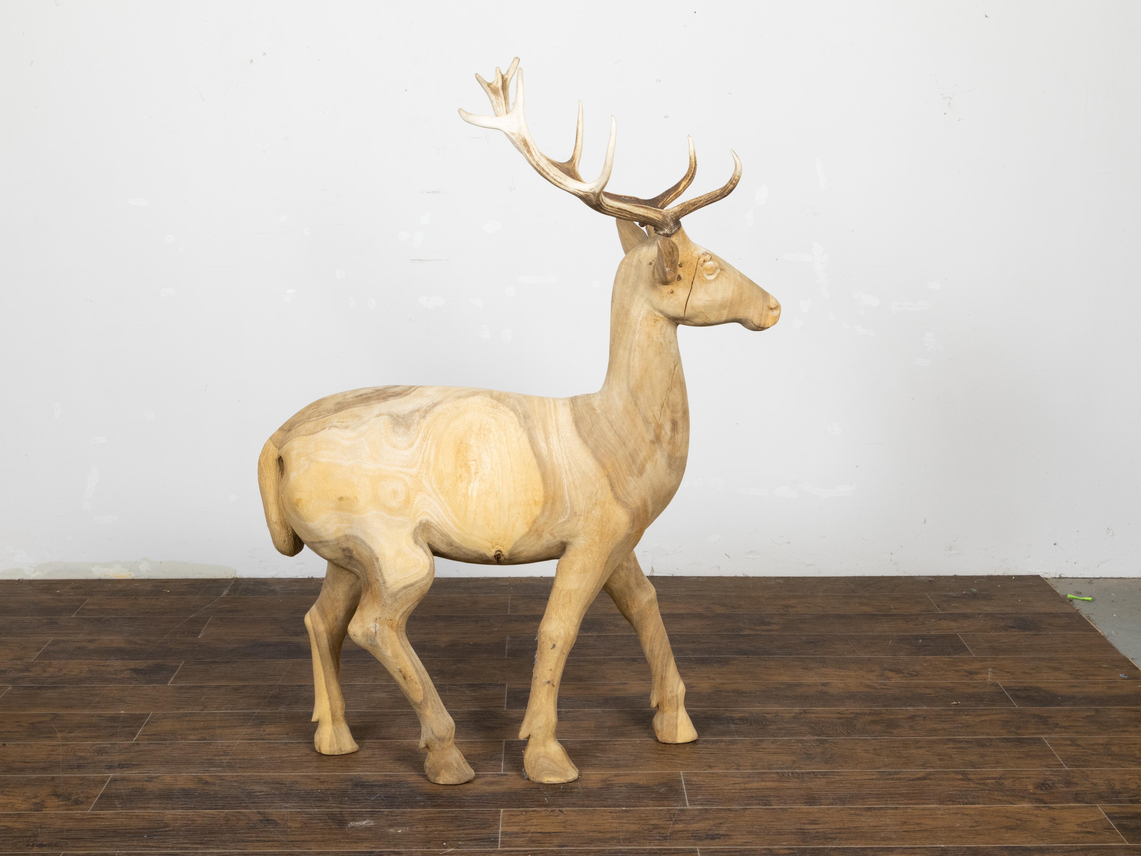 A life-size sculpture of a stag from the mid 20th century with antlers and natural patina. Hand-carved during the Midcentury period, this sculpture charms us with its life-size depiction of a majestic walking stag. Boasting a natural patina