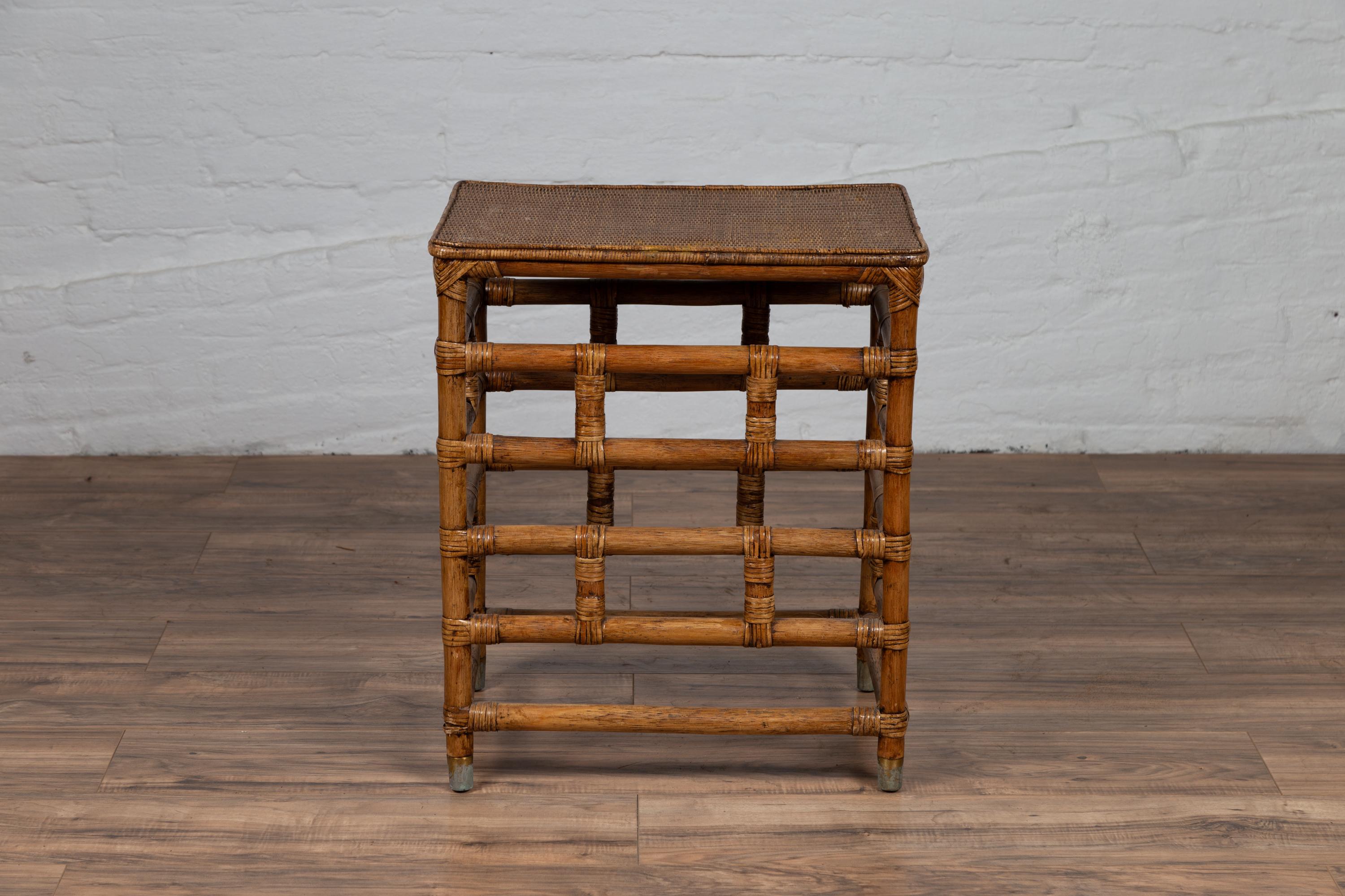 A vintage Thai bamboo side table from the mid-20th century, with rattan top. Born in Thailand during the mid-century period, this stylish side table features a linear silhouette made of a geometrically organized bamboo base. Surmounted by a rattan