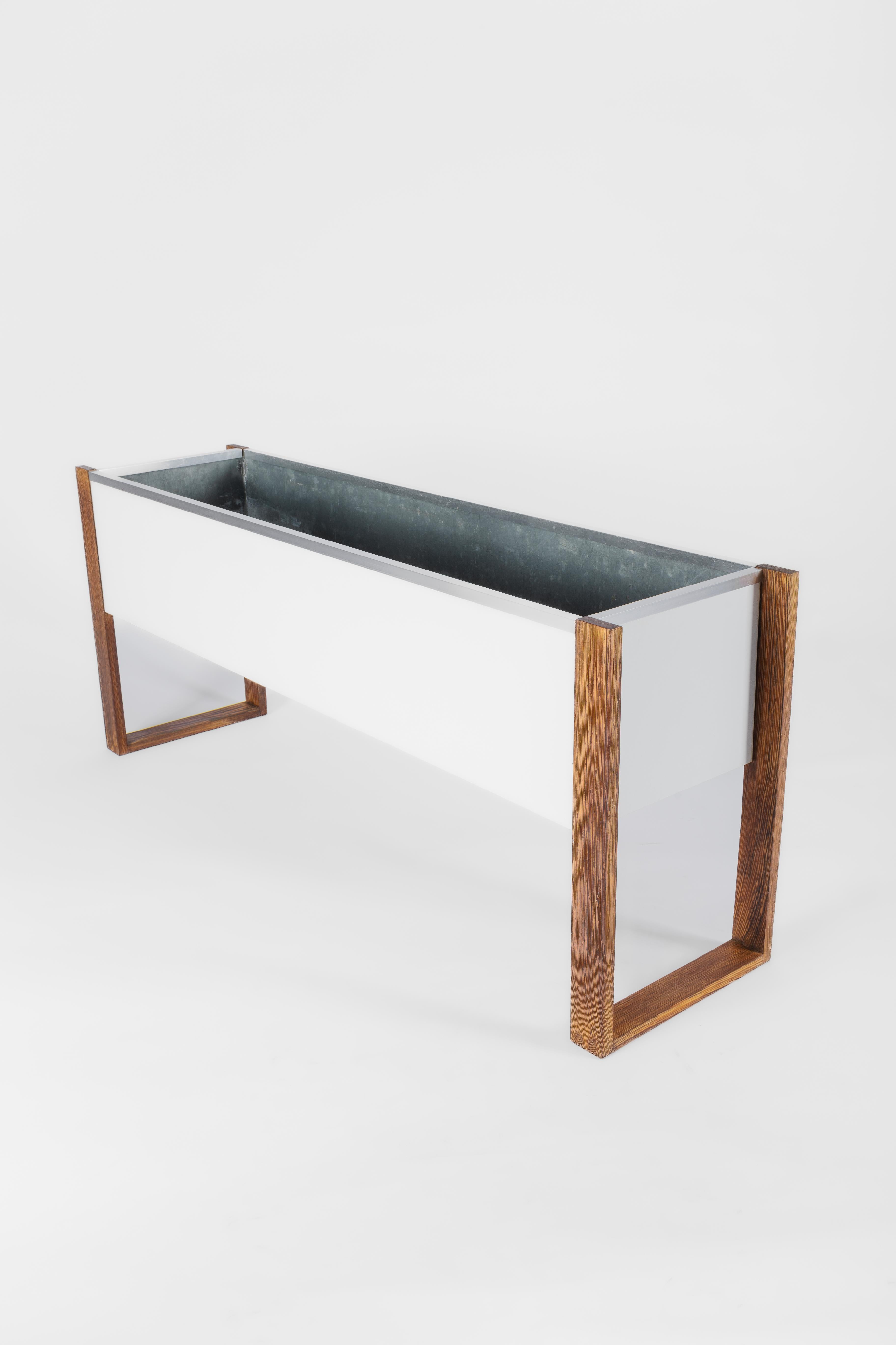 Midcentury indoor planter

Made by the belgian firm Beaufort.

Made in a combination of Wengé wood, chrome and white melamine.

The inside is the original zinc planter, which protects the fragile wood from the water.

The wengé wood has been cleaned