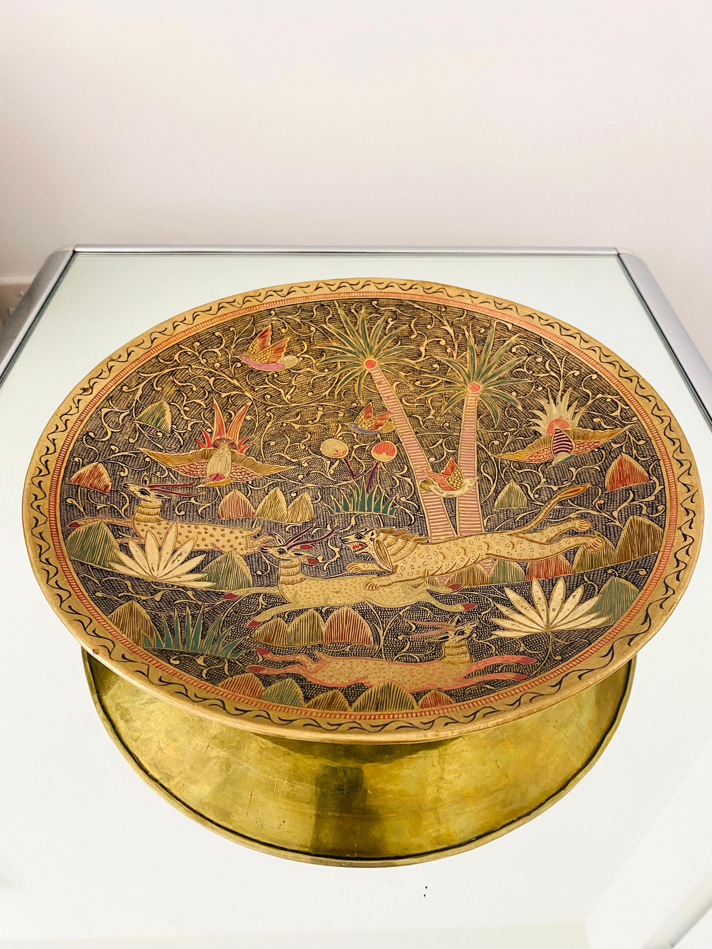 Decorative brass plate or vide-poche dish with engraved scene featuring exotic animals and plants and islamic scroll motifs along the border. The dish features hand-painted enameled inlays in hues of red, green, brown, and black. This is a hand