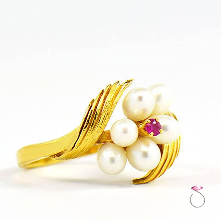 Vintage Mikimoto flower Ring in 18K yellow gold with 6 Akoya White Pearls and Ruby center. This beautiful flower cluster design ring features 6 grade a white pearls. The design features 6 oval Akoya white pearls surrounding a red ruby center. The