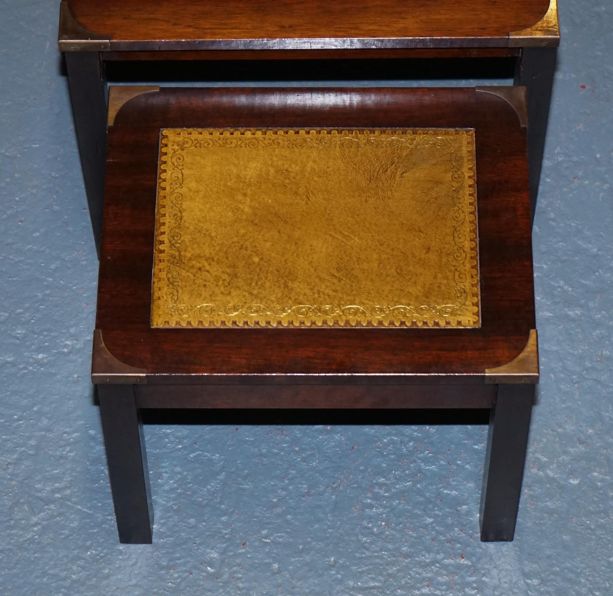 
Antiquités de Londres



Un ensemble distingué de trois tables gigognes Campaigner vintage, fabriquées en bois dur riche et dotées d'inserts en cuir estampé encadrés par des montures d'angle en laiton massif - un clin d'œil au design militaire