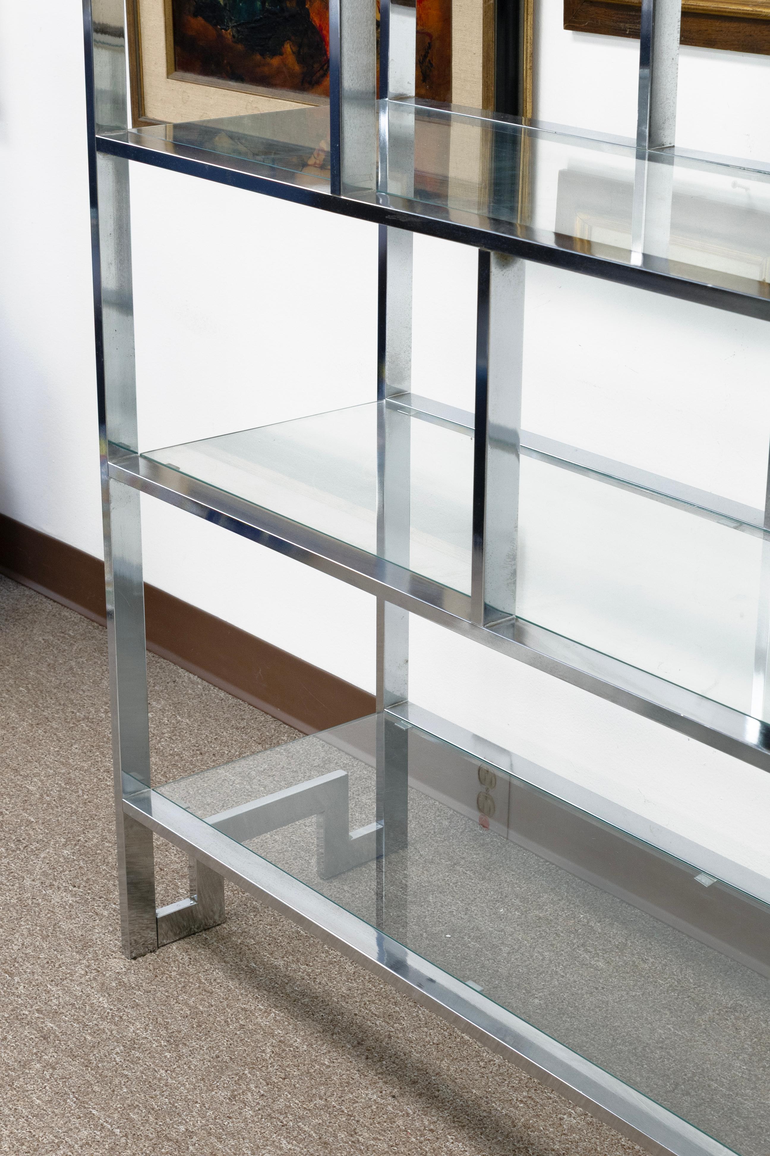 A striking Mid-Century Modern étagère designed by Milo Baughman, featuring a polished chrome frame with clean, geometric lines and multiple tiers of clear glass shelving. The asymmetrical design creates an architectural presence, offering both open