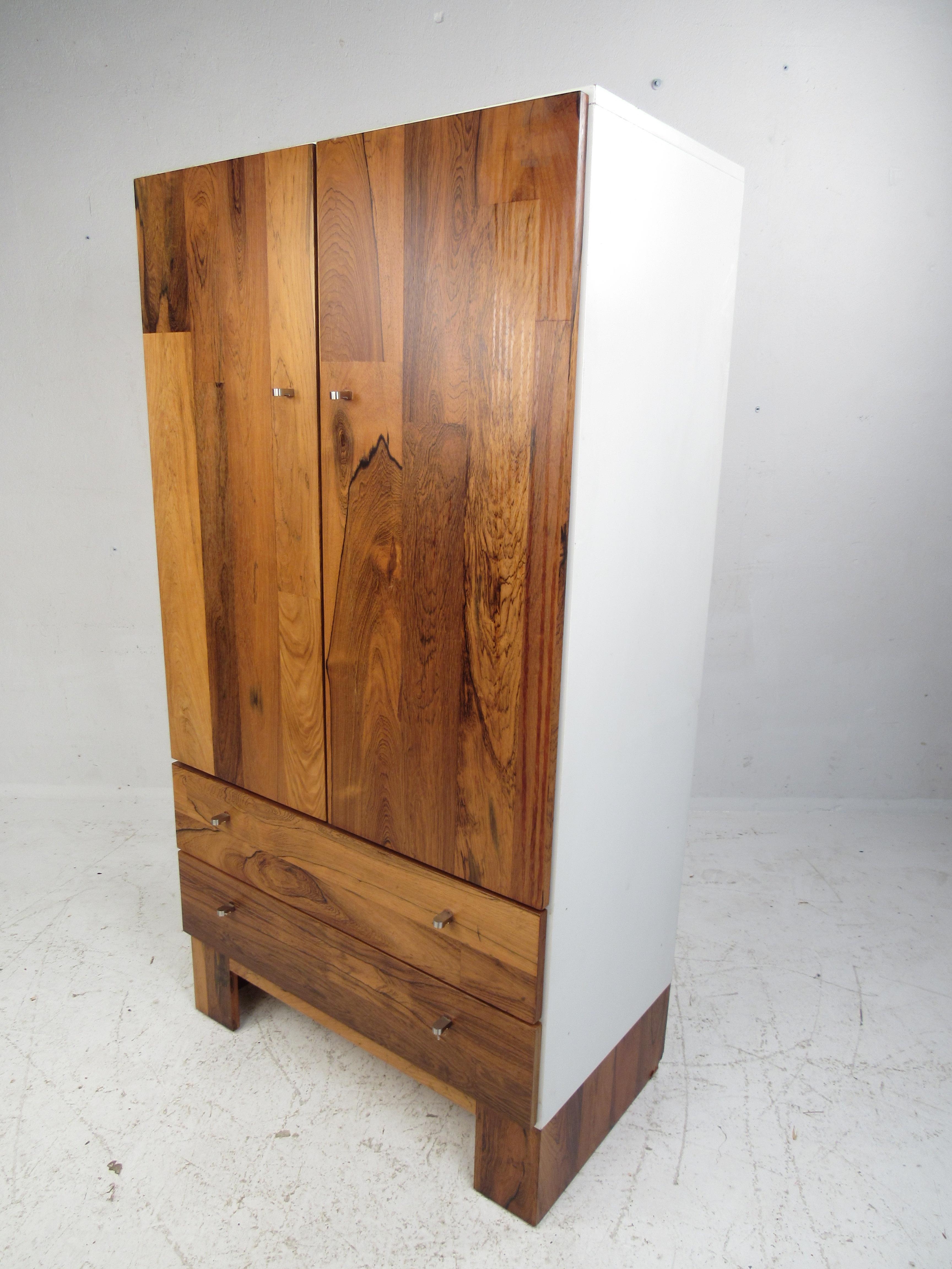 This beautiful Mid-Century Modern armoire boasts a rich rosewood front and a white casing. The lovely two-tone design with uniquely shaped chrome pulls and a white interior easily complements any bedroom. A stylish case piece with plenty of room for