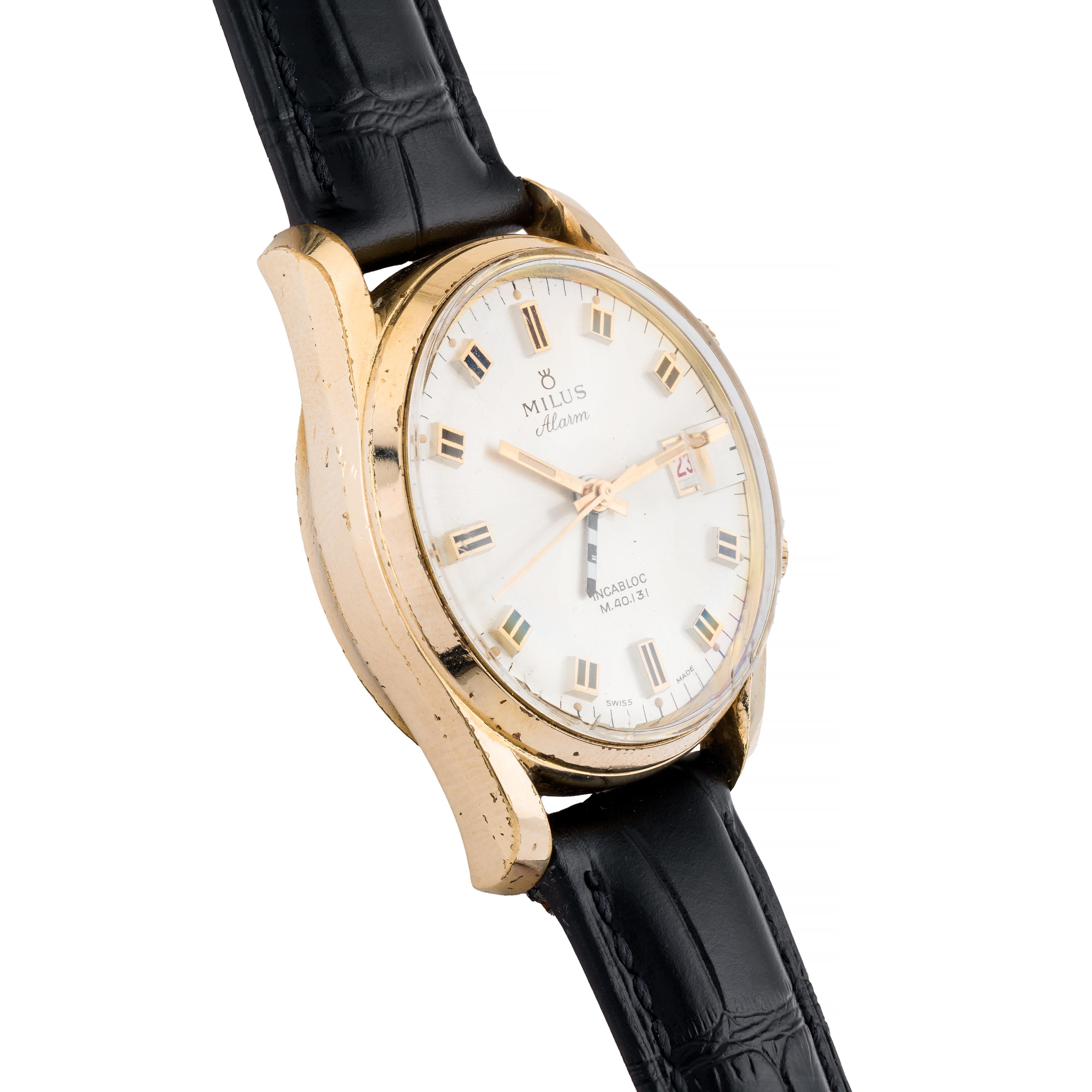 Aston Estate Jewelry Presents:

A vintage Milus Alarm wristwatch crafted in gold-filled.

The round watch features a clean silver dial with bold rectangular hour markers and a date window at 3 o'clock. The dual crowns add functionality, with one