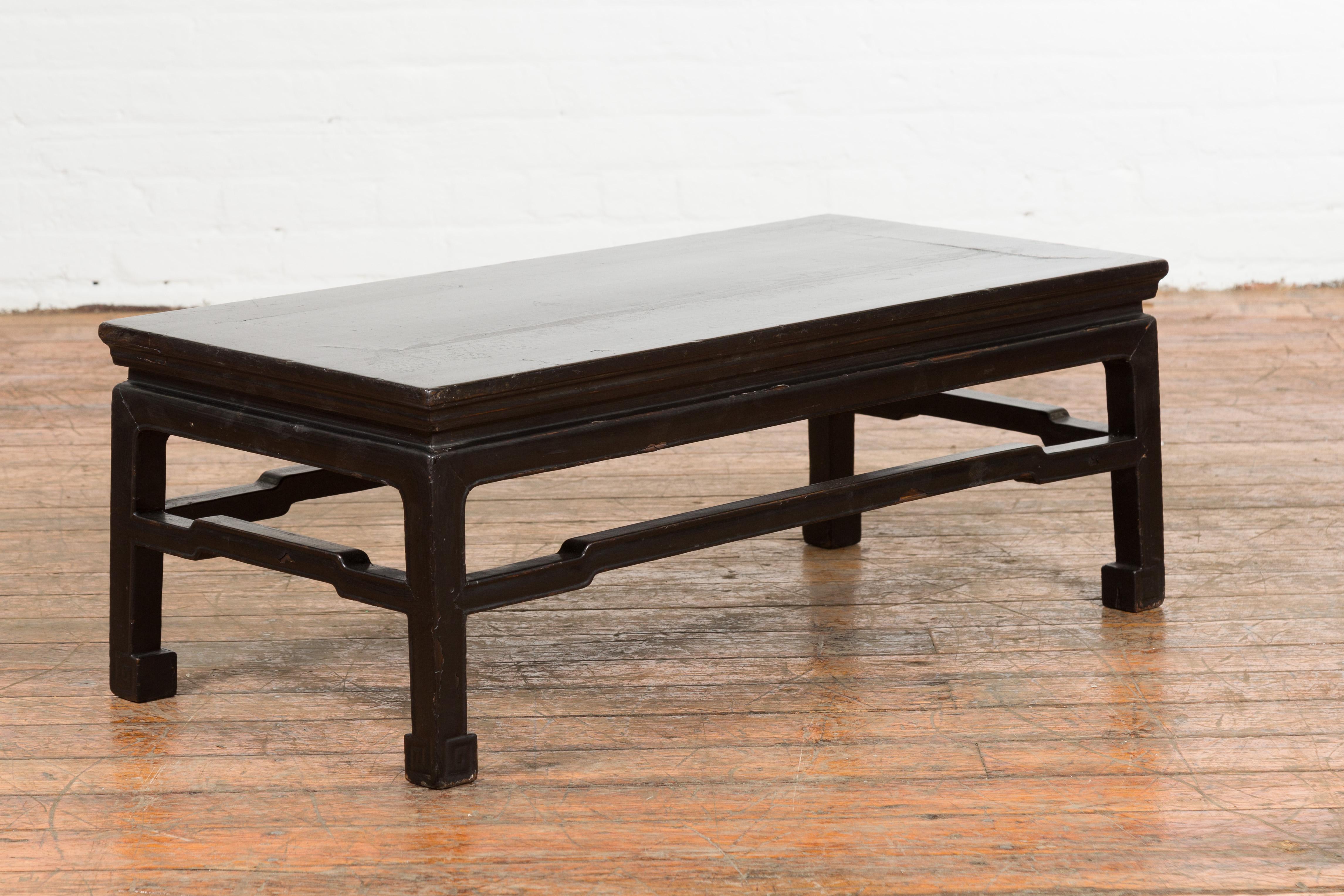A Chinese Ming Dynasty style vintage black lacquer coffee table from the mid 20th century, with horse hoof legs and humpback stretchers. Created in China during the midcentury period, this black lacquer coffee table features a rectangular waisted