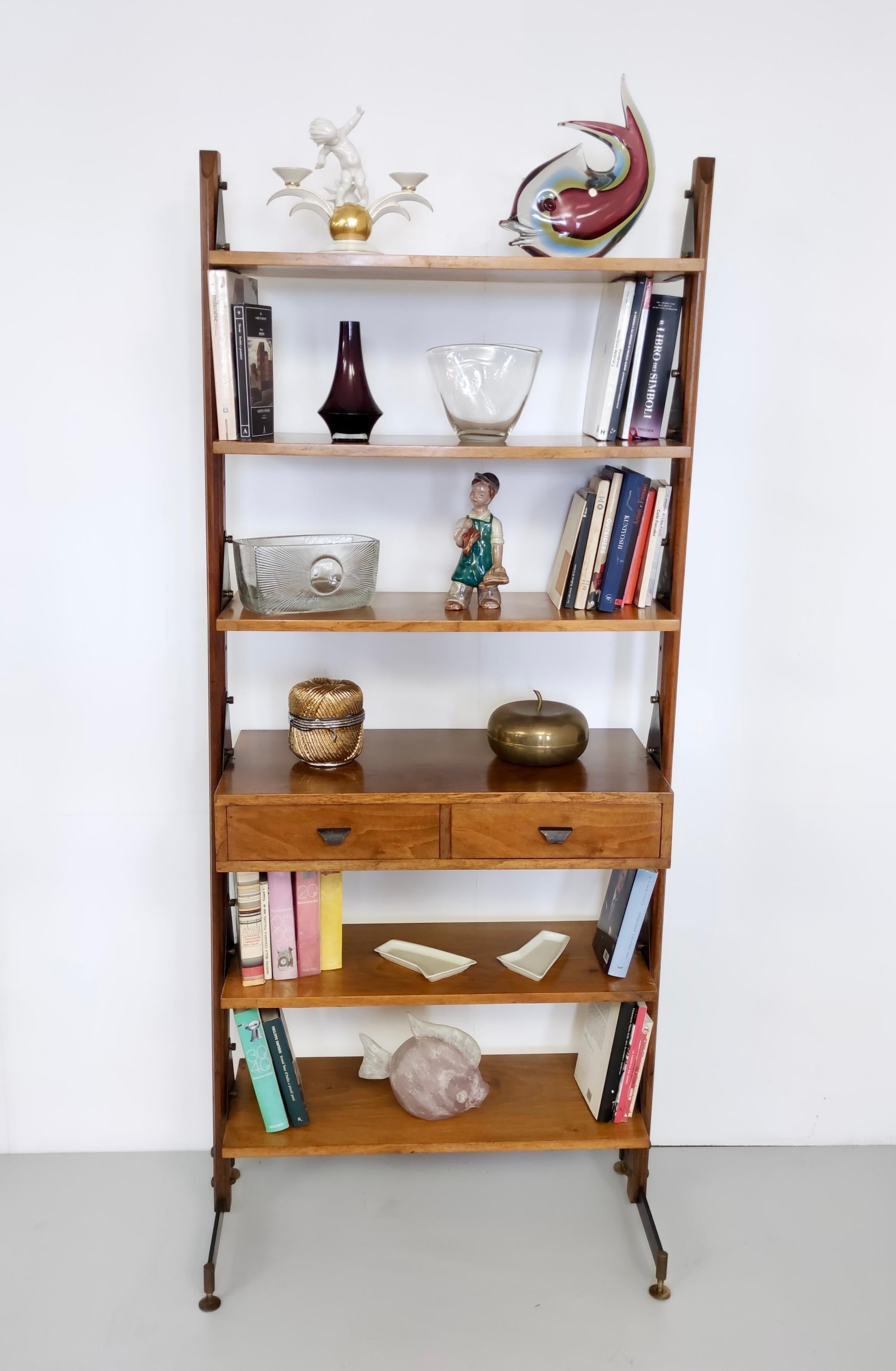 Made in Italy, 1970s.
This bookshelf is made in walnut and features a varnished metal frame with brass feet caps and details.
It may show slight traces of use since it's vintage, but it can be considered as in very good original condition and ready
