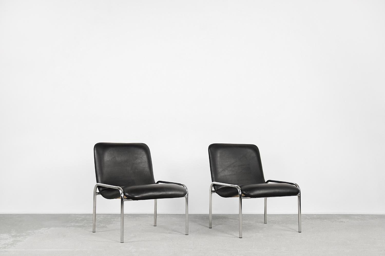 Este conjunto de dos sillones fue fabricado por la empresa alemana Thonet en la década de 1970. El armazón es de acero tubular cromado. Las sillas están hechas de madera contrachapada y revestidas de piel sintética negra. La forma minimalista aporta