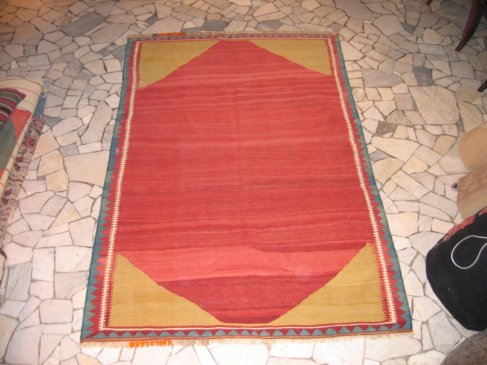 A highly graphic tribal Kilim decorated by a large hexagonal open field cartouche in various shades of red laid over a pistachio green background, of which we see only the corner elements. Flat weaves of this type are highly coveted because its