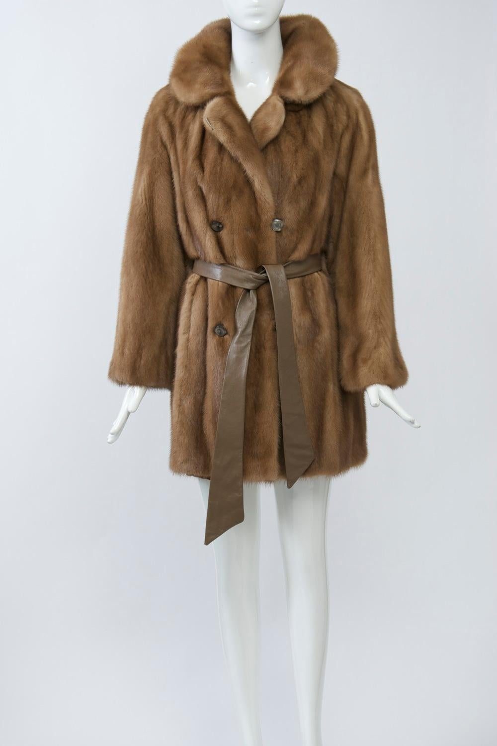Golden mink jacket, c.1970s, featuring double-breasted styling and a leather sash belt that passes through the side seams to tie in front and leave the back loose (can also be sashed around the entire waist). The collar can be buttoned up for