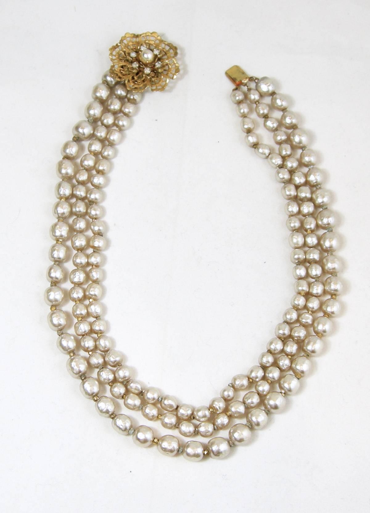This vintage Miriam Haskell necklace has a slide in clasp with an open gold tone floral design with small rhinestone around a faux pearl center.  There are 2 strands of small faux baroque pearls with gold tone space between each pearl and the third