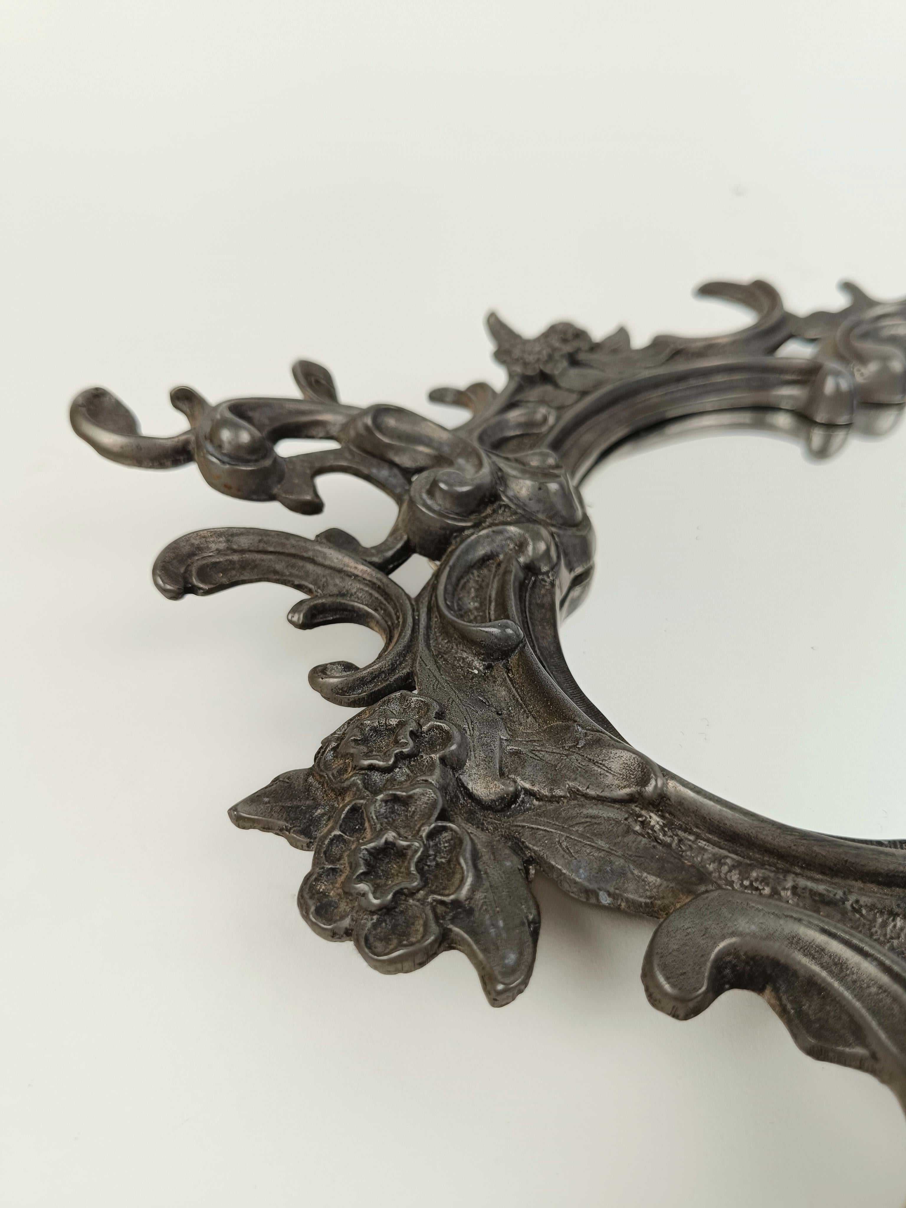 Un miroir vintage fabriqué autour de la première moitié du 20e siècle mais dans le style des miroirs antiques européens du 18e siècle dans le style baroque ou rococo.
La structure de forme irrégulière et sinueuse est en argent allemand ciselé à la