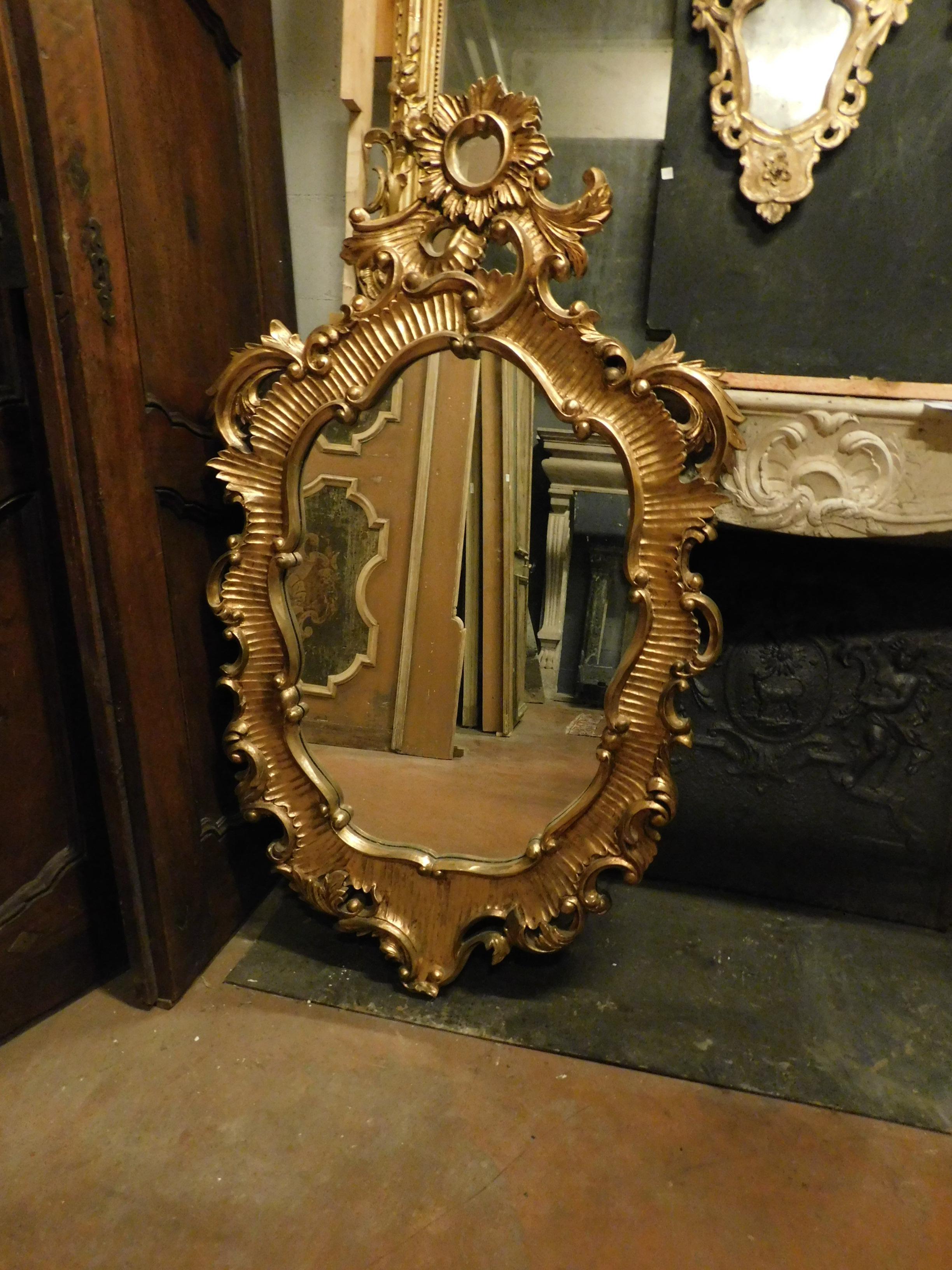 Vintage mirror in carved and gilded wood, molded frame with a shaped shape around which leaf shoots are wrapped that from the lower center move symmetrically upwards to form the large sunburst molding, particular shape, very baroque and of great