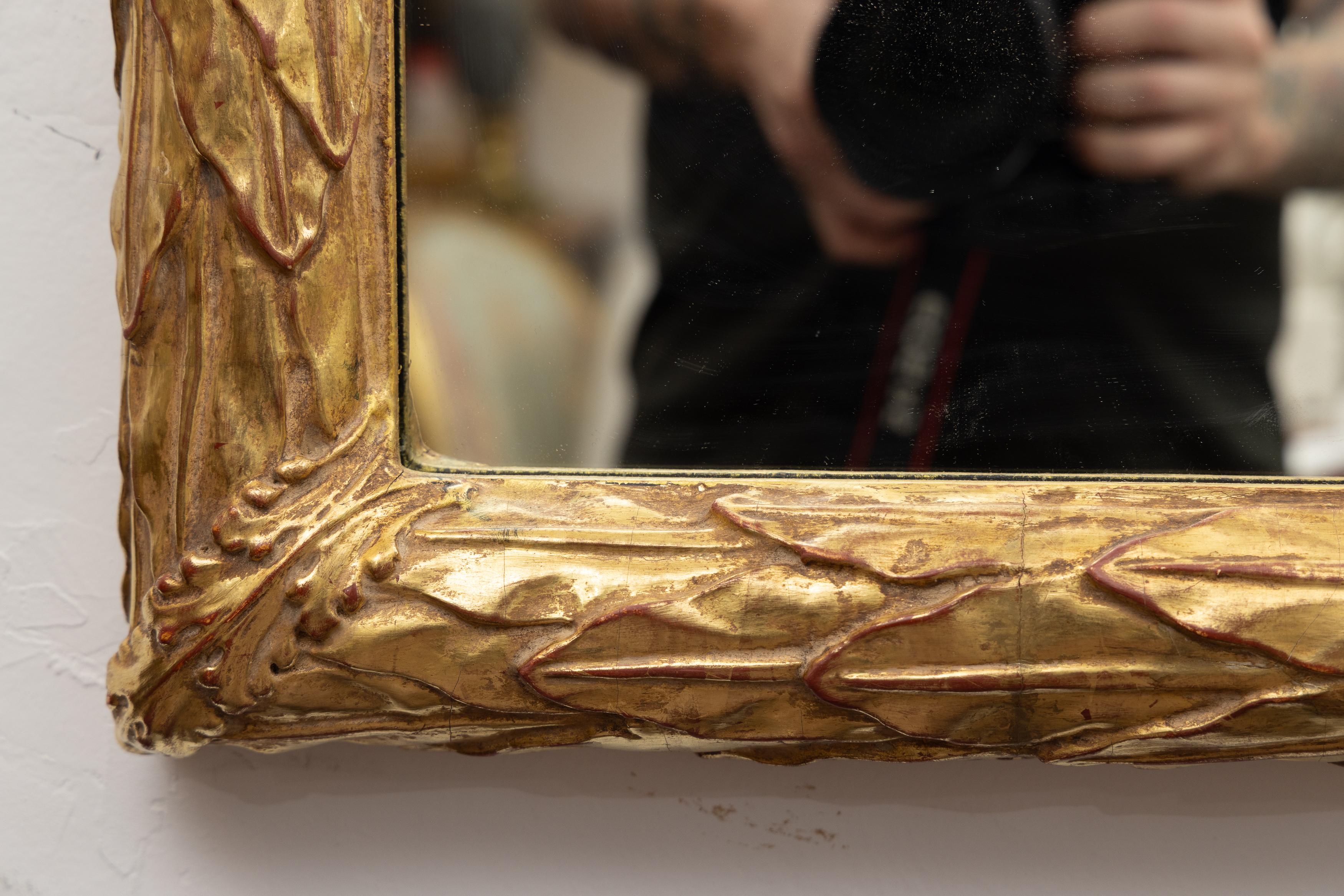 Il s'agit d'un miroir rectangulaire simple, mais élégant, avec une plaque entourée d'un cadre doré à l'eau représentant artistiquement un feuillage sculpté en cascade.