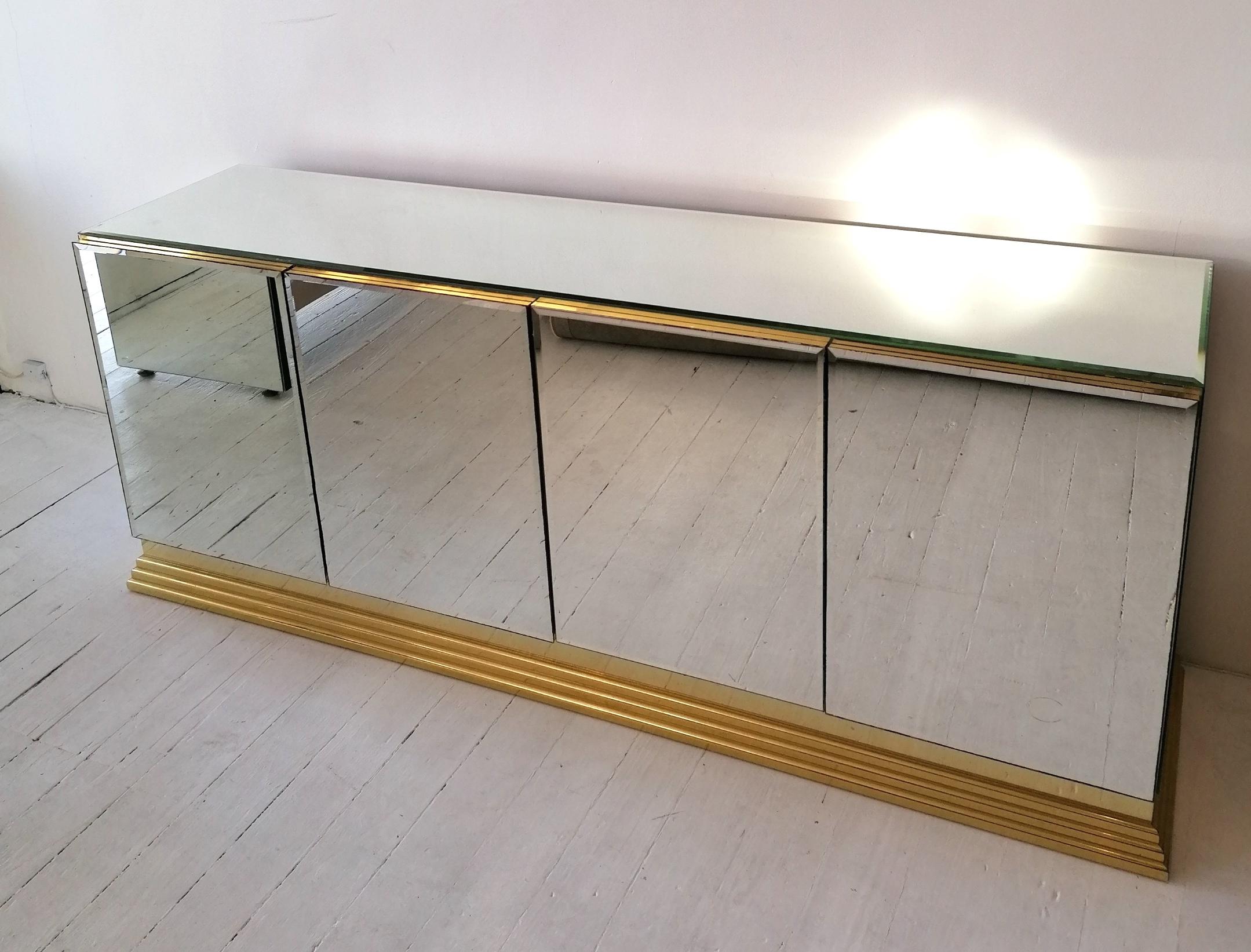 A beautiful vintage mirror glass sideboard by Ello, USA, circa late 1970s/early 80s. This simple & elegant design has a shaped brass metal base. The ends of the cabinet are mirror glass; the top is bevelled mirror glass, as are the door fronts.