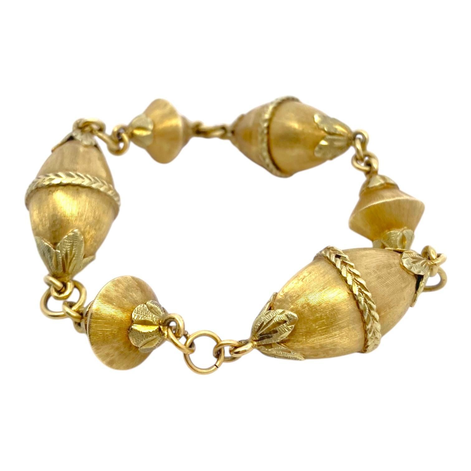 Vintage 18K yellow gold link bracelet, featuring a series of acorn-shaped links with intricate leaf motifs. Each link is crafted with a satin textured finish and braided detailing, adding depth and elegance. The bracelet is connected by gold rings,
