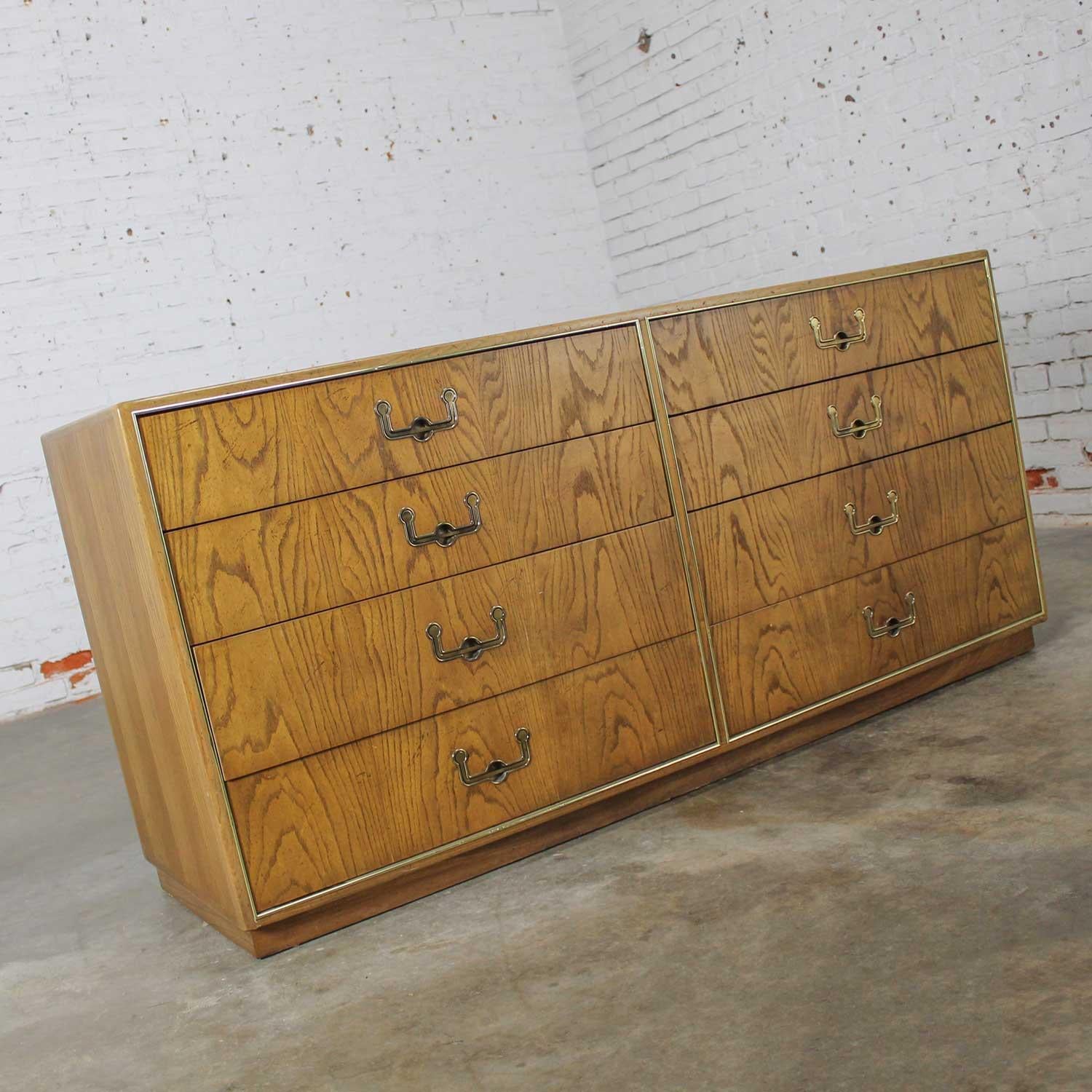 Wonderful vintage modern campaign style dresser by Founders Furniture comprised of book matched oak veneer & eight drawers with antique brass toned hardware and brass plated beading details. Beautiful condition, keeping in mind that this is vintage