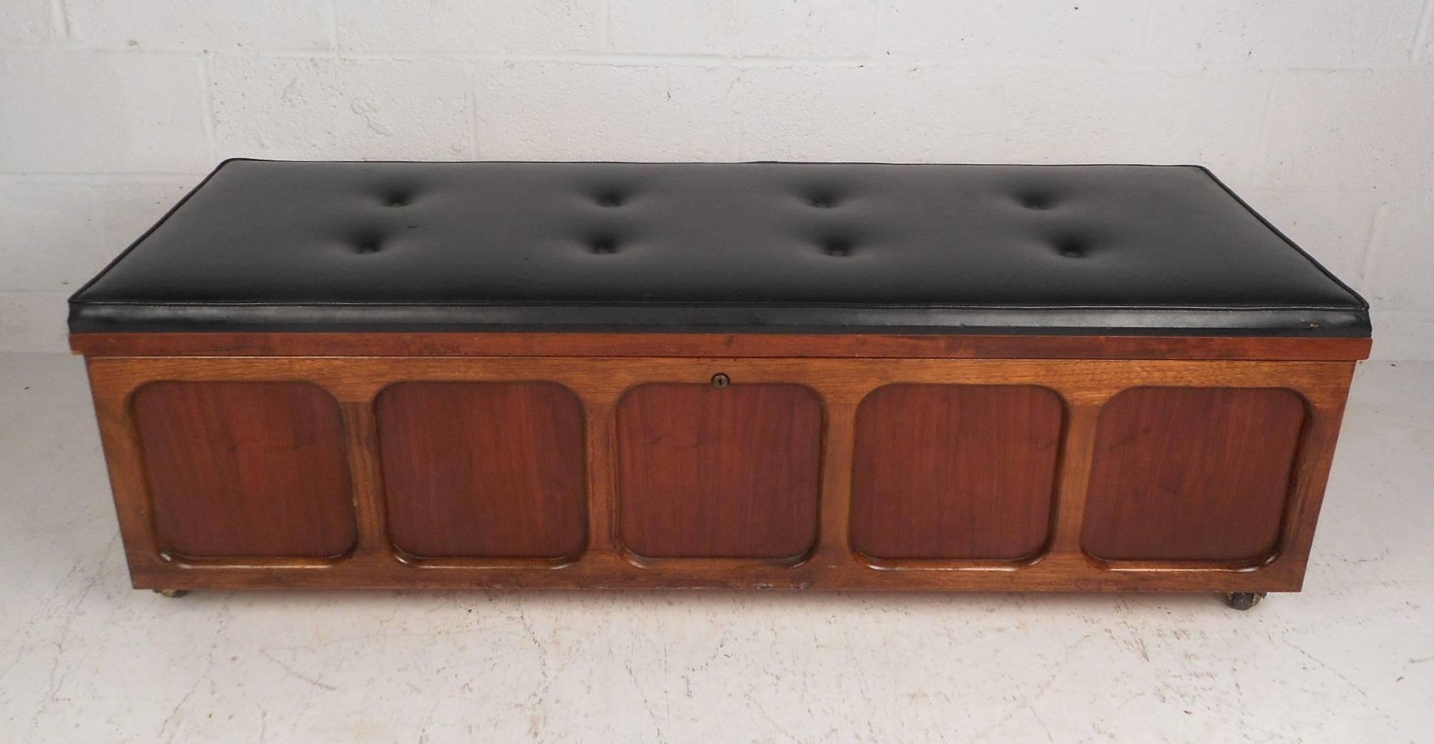 A beautiful Mid-Century Modern cedar chest with a thick padded cushion on top covered in black tufted vinyl. Quality construction with a unique embossed design on the front, four castors for convenience, and a finished back. This versatile piece