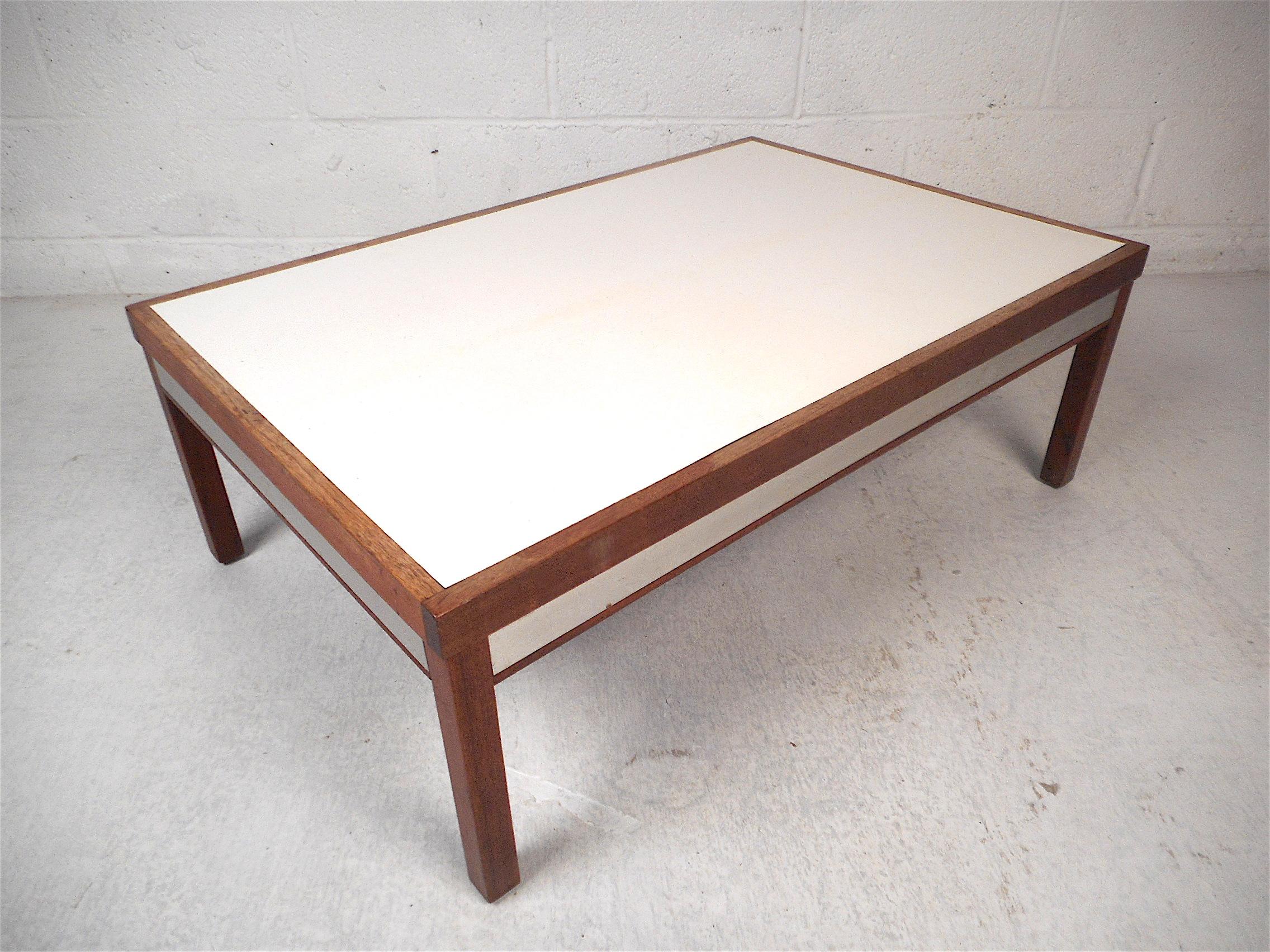 Interesting midcentury coffee table, white laminate table surface, metal trim on the sides, along with a sturdy wooden frame. A compact table perfect for apartment living. This table is sure to make a great addition to any modern interior. Please