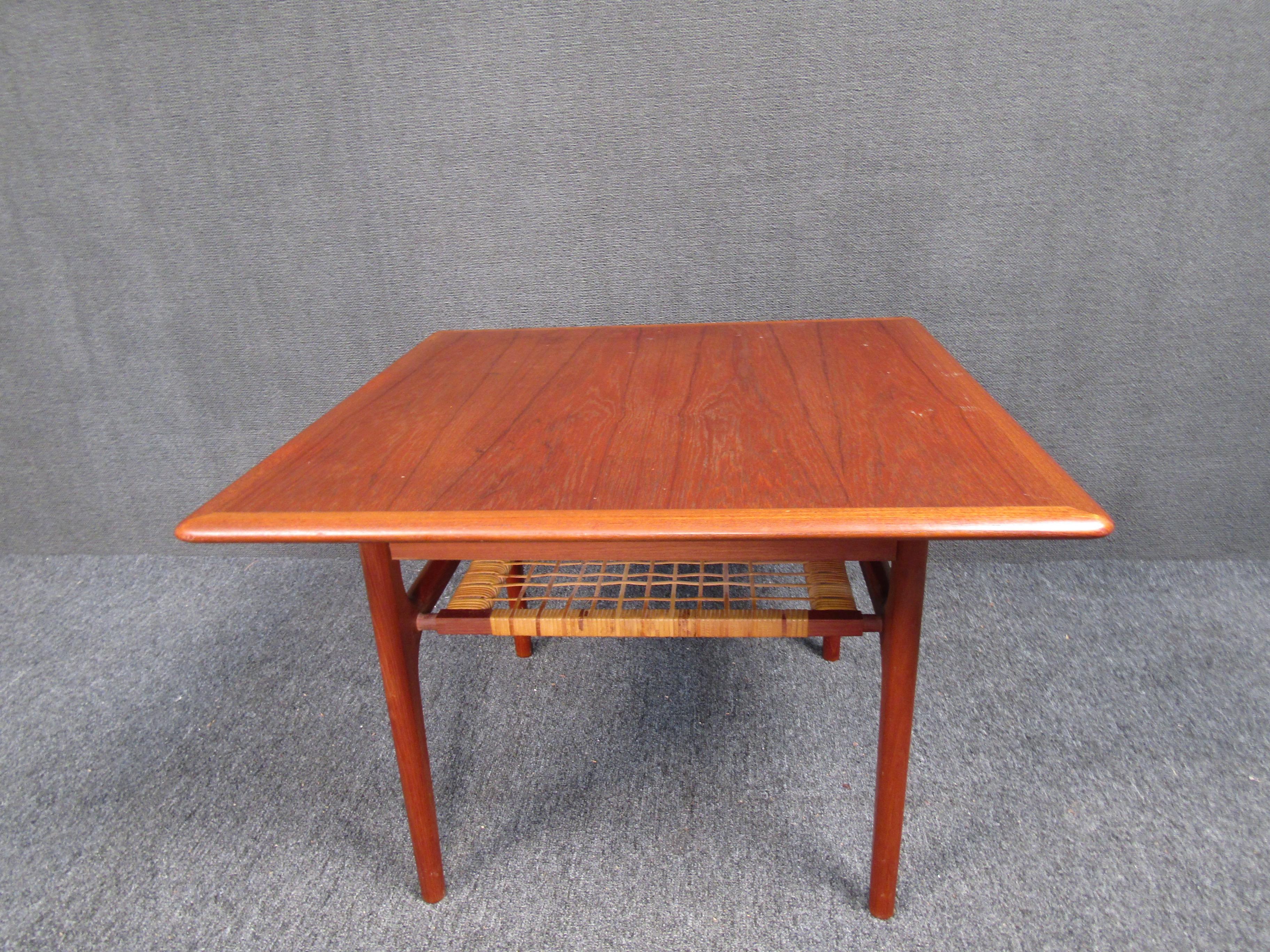 This fabulous Mid-Century Modern end table features a lower slatted tier for added storage. The sleek design was made in Denmark and has elegant teak wood grain throughout. This lovely end table have smooth rounded edges and a rectangular top. A