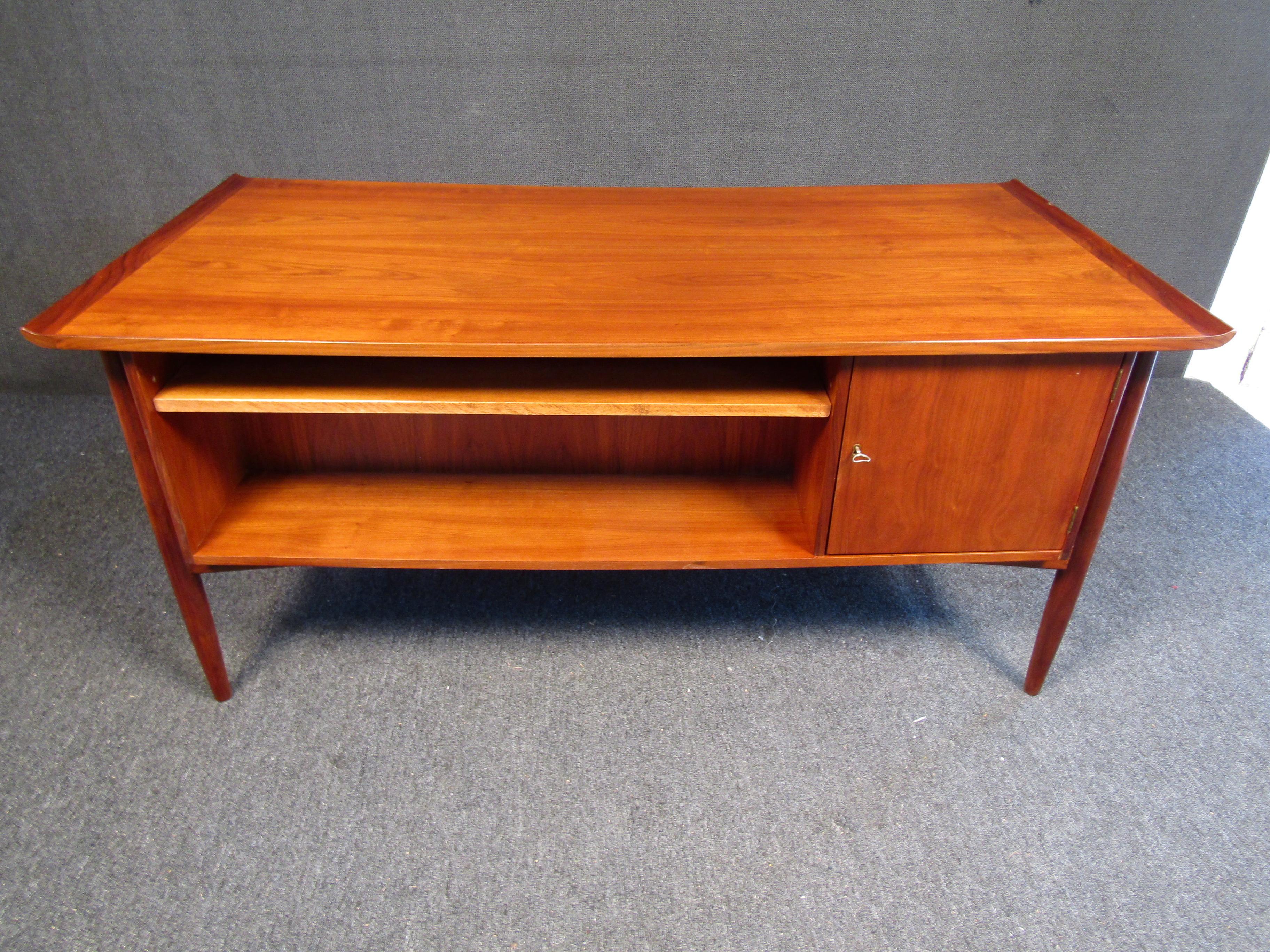 This vintage danish executive desk in teak features a raised sculpted top and tapered legs. This versatile piece can be showcased from all angles and includes a backside shelf and cabinet compartment, as well as four drawers in the front to