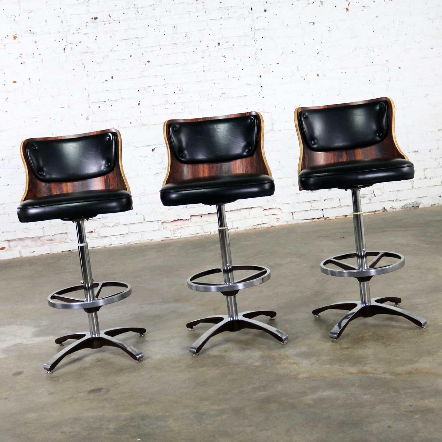Handsome set of 3 vintage modern adjustable bar stools in laminate and black vinyl with chrome and cast aluminum bases by Daystrom. These stools adjust from bar height to counter height and swivel 360 degrees. They are in overall wonderful vintage