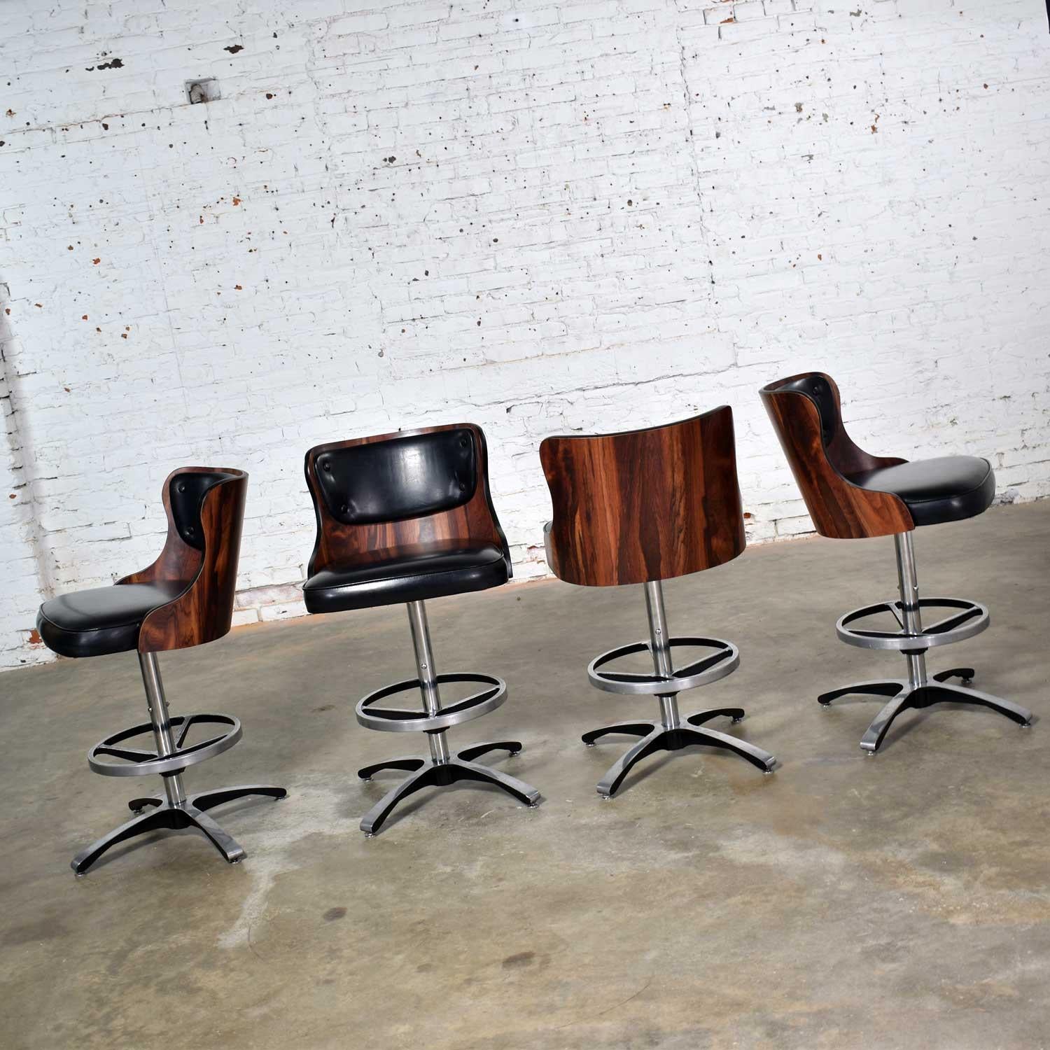 Handsome set of 4 vintage modern adjustable bar stools in laminate and black vinyl with chrome and cast aluminum bases by Daystrom. These stools adjust from bar height to counter height and swivel 360 degrees. They are in overall wonderful vintage