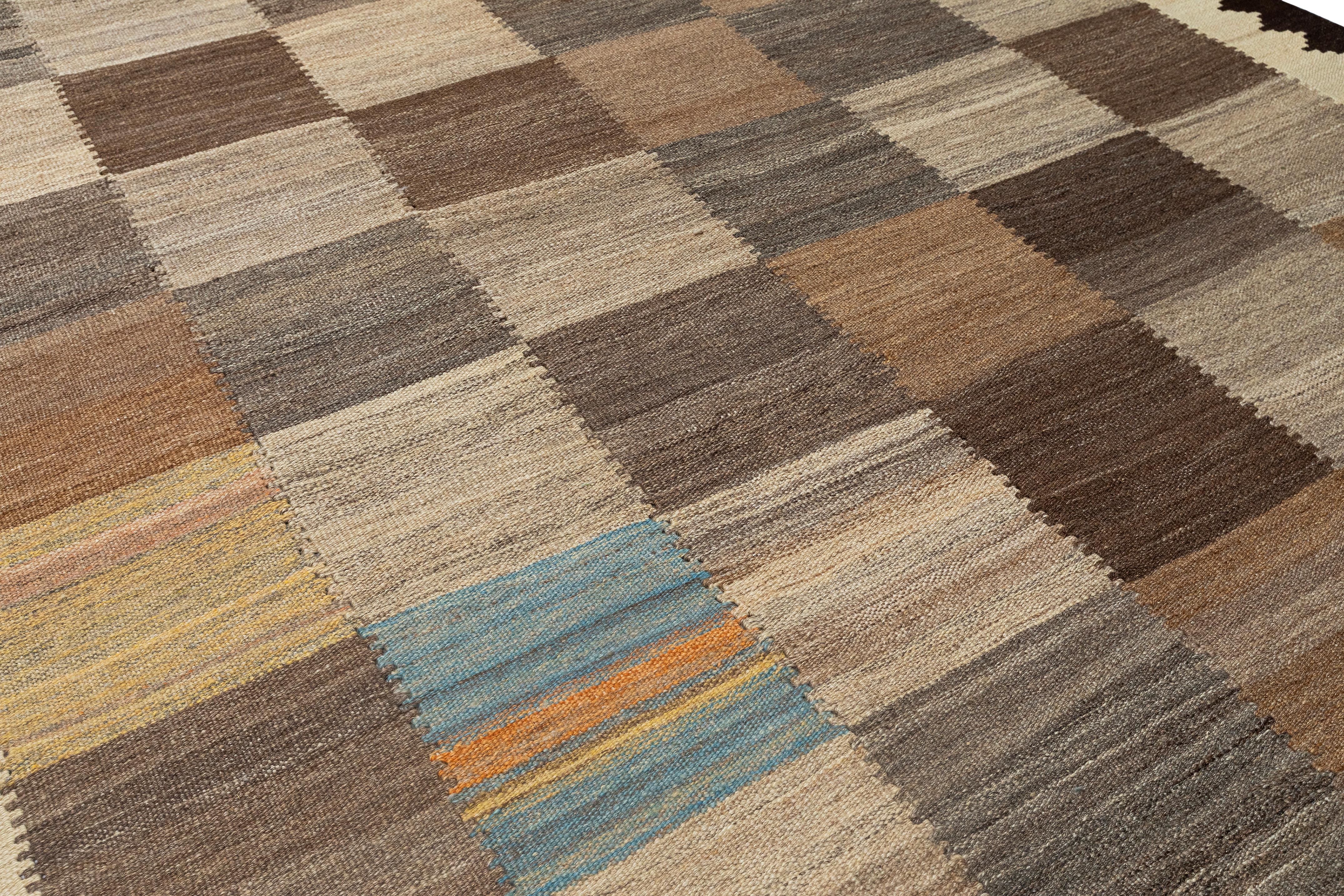 Questo tappeto kilim moderno a tessitura piatta è caratterizzato da un disegno a griglia splendidamente bilanciato composto da blocchi neutri di colore tortora, beige, marrone e sottili accenti di azzurro. Il layout è incorniciato da audaci bordi