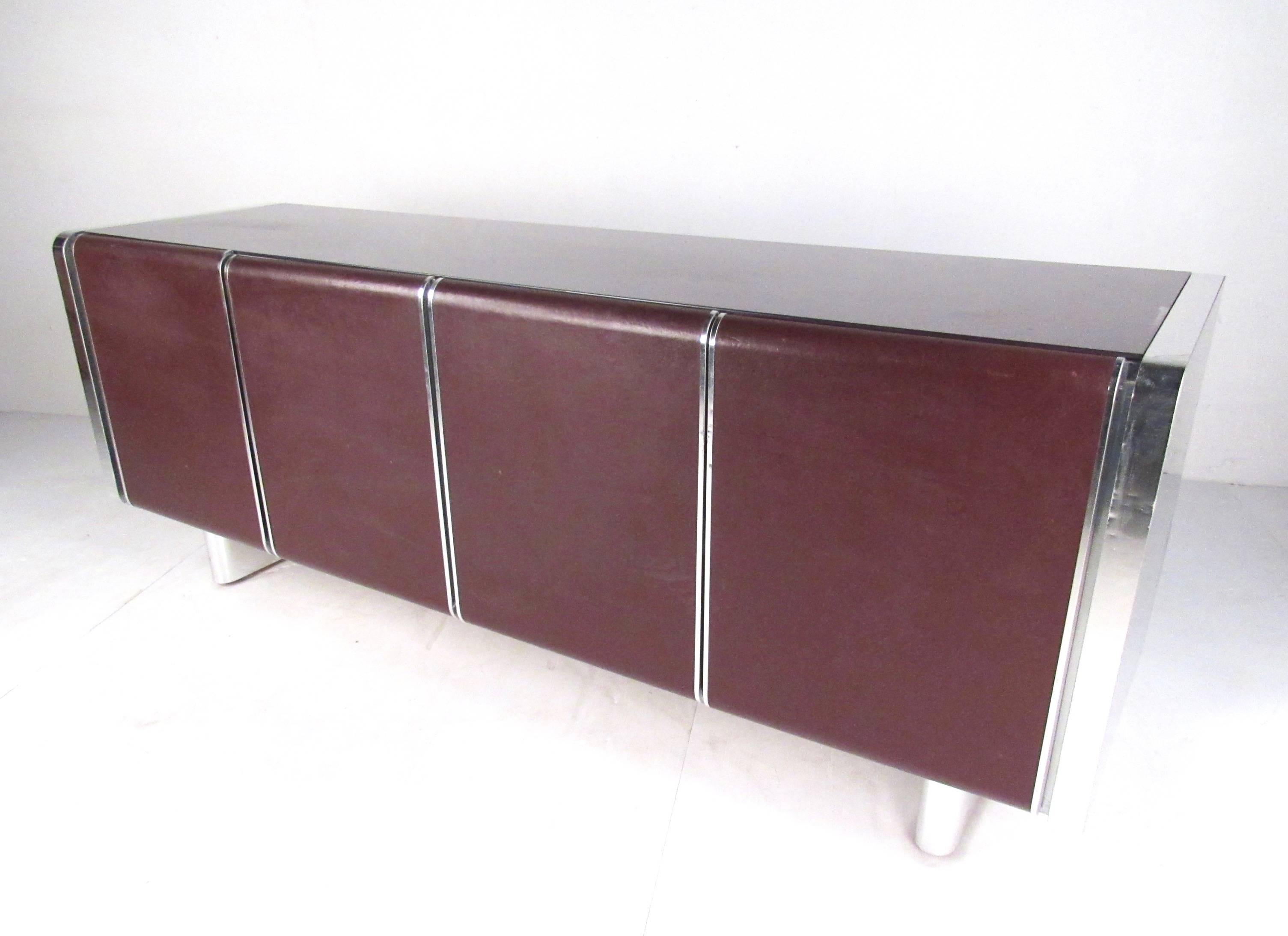 This retro modern sideboard features midcentury style including chrome casing, leather door fronts, and glass top. Spacious interior cabinets allow for adjustable shelves and versatile storage as a living room credenza, dining room sideboard, or