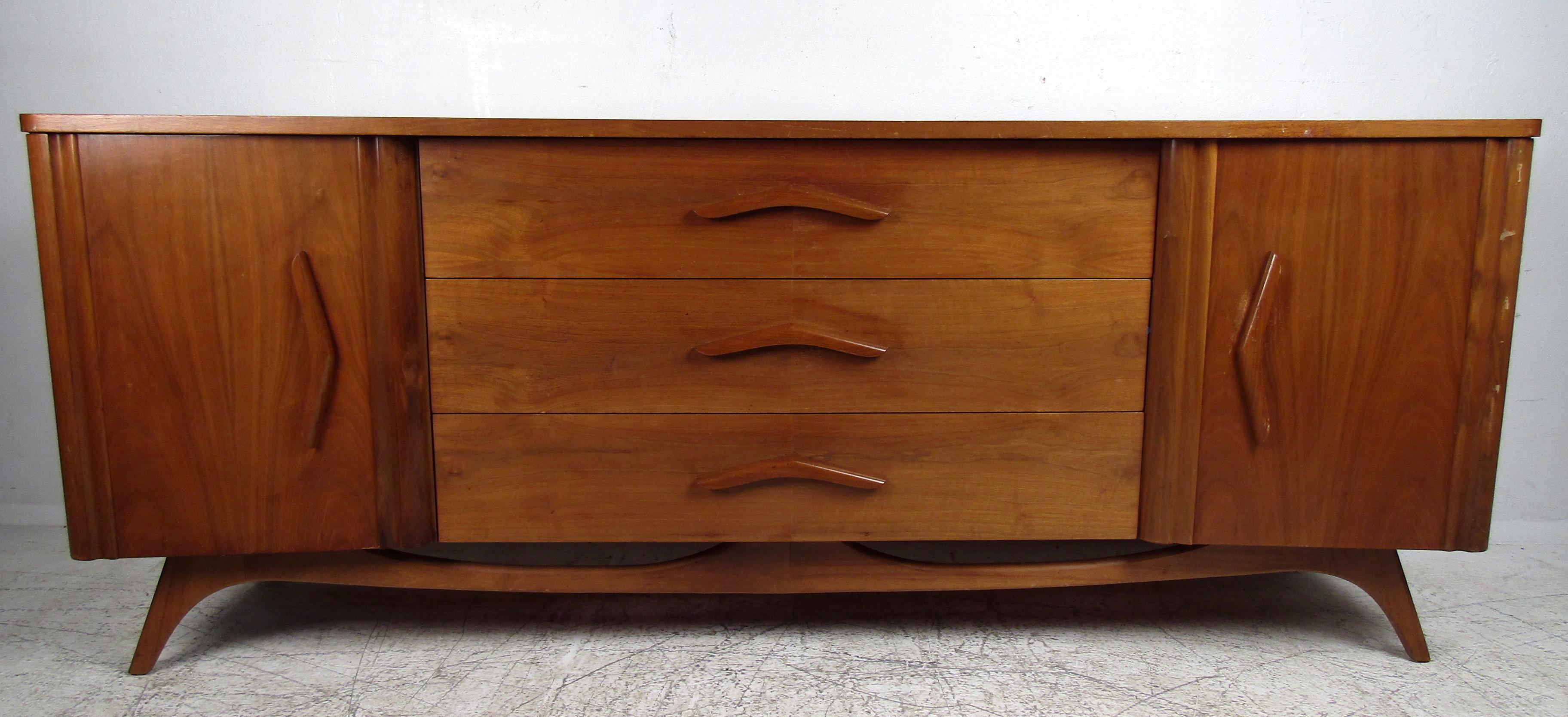 Sleek Mid-Century Modern lowboy dresser featuring three large spacious drawers with sculpted pulls, six hidden drawers, on a set of sturdy legs in rich walnut grain.

Please confirm the item location (NY or NJ).
  