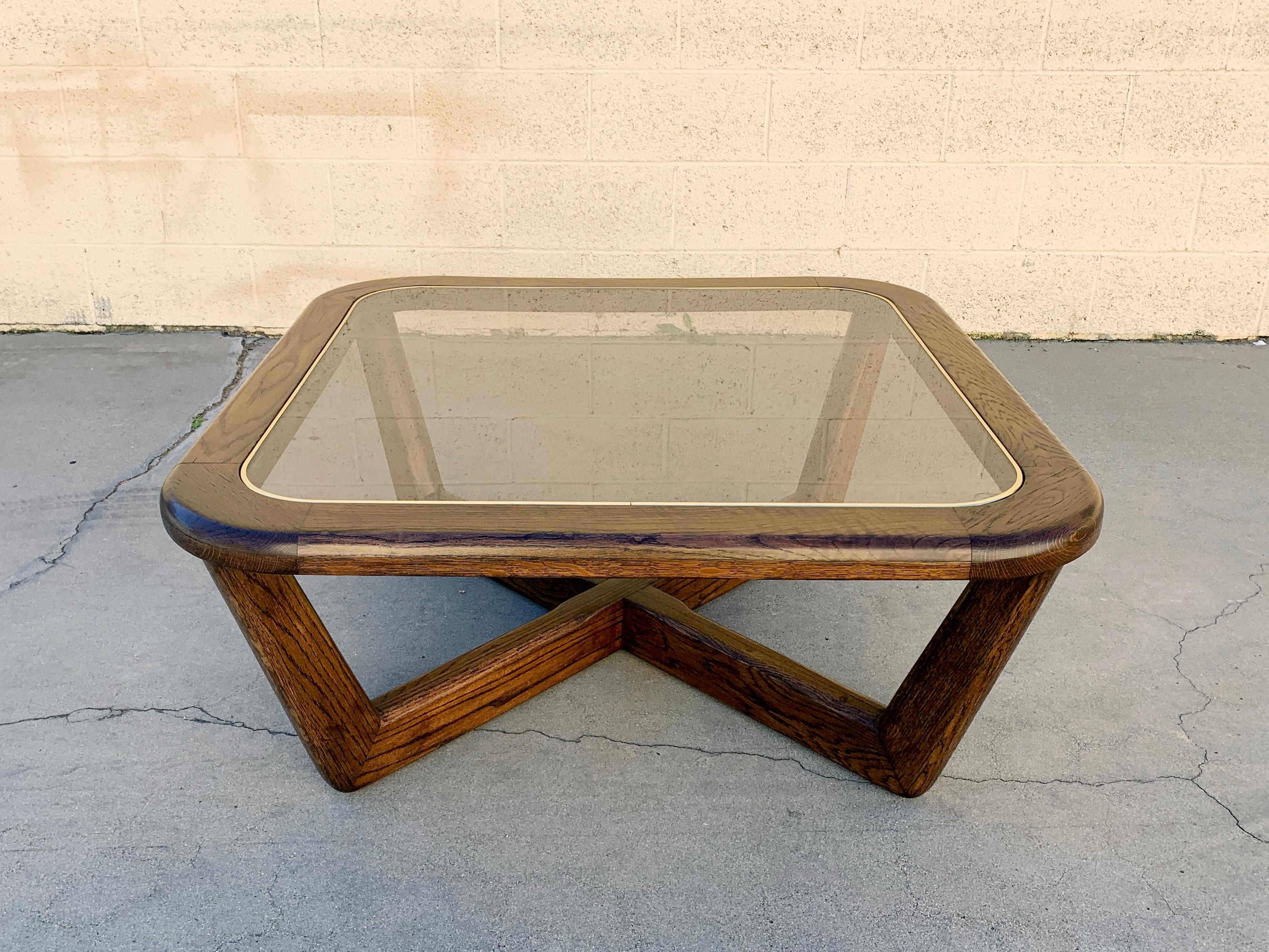 Late 1970s-early 1980s modern coffee table made of solid oak with lacquered walnut stain. Geometric base holds an inlaid glass top with brass coated rubber trim. Great geometric styling. Glass shows some wear; please note some scratches and a