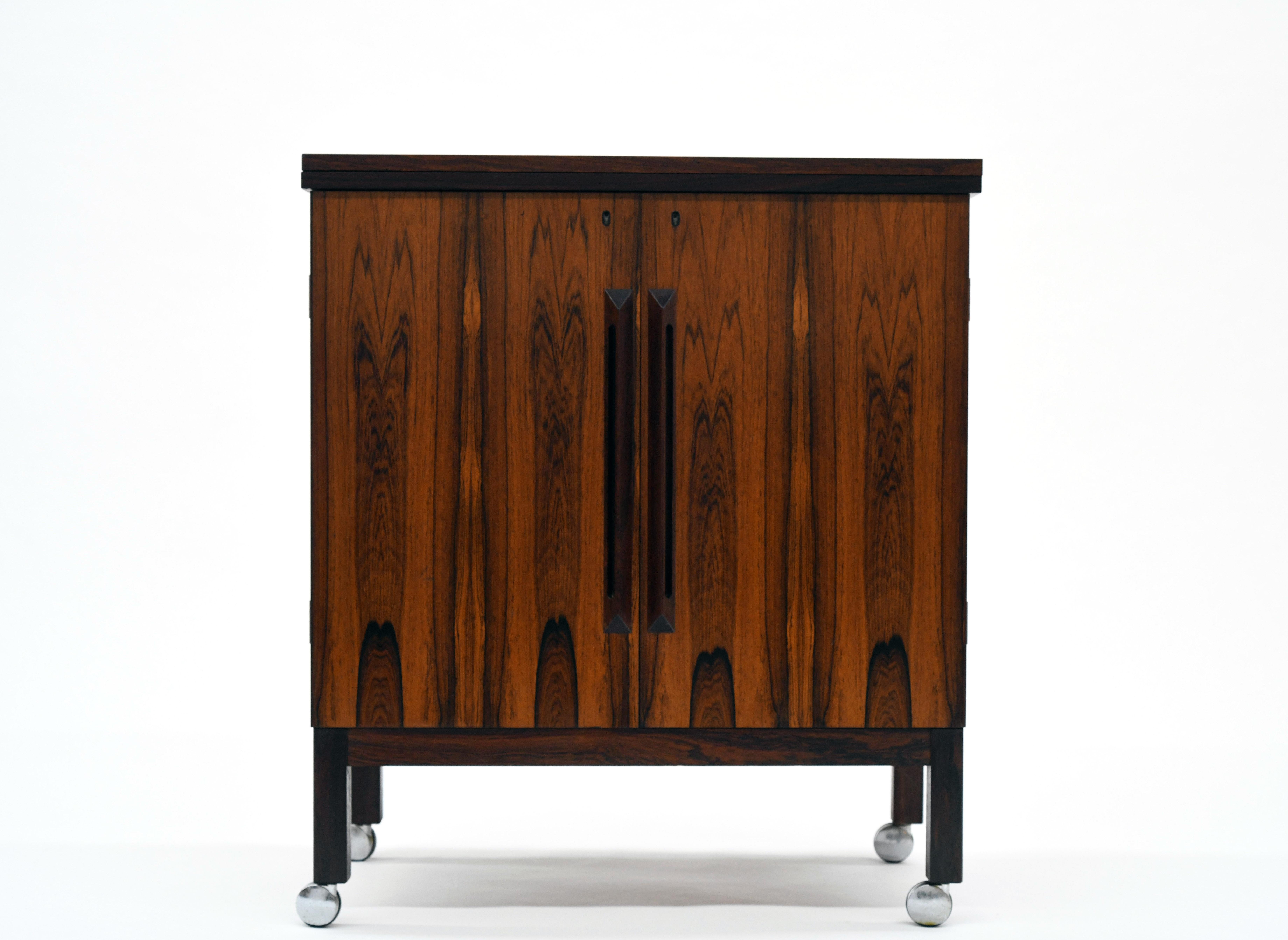 Attractive and functional flip-top bar cabinet in Brazilian rosewood. High quality construction throughout. Locking cabinet opens to reveal storage for all necessary bar accoutrements. Black laminate flip-top measures 60.5 W x 16.25 D x 34.75 H when