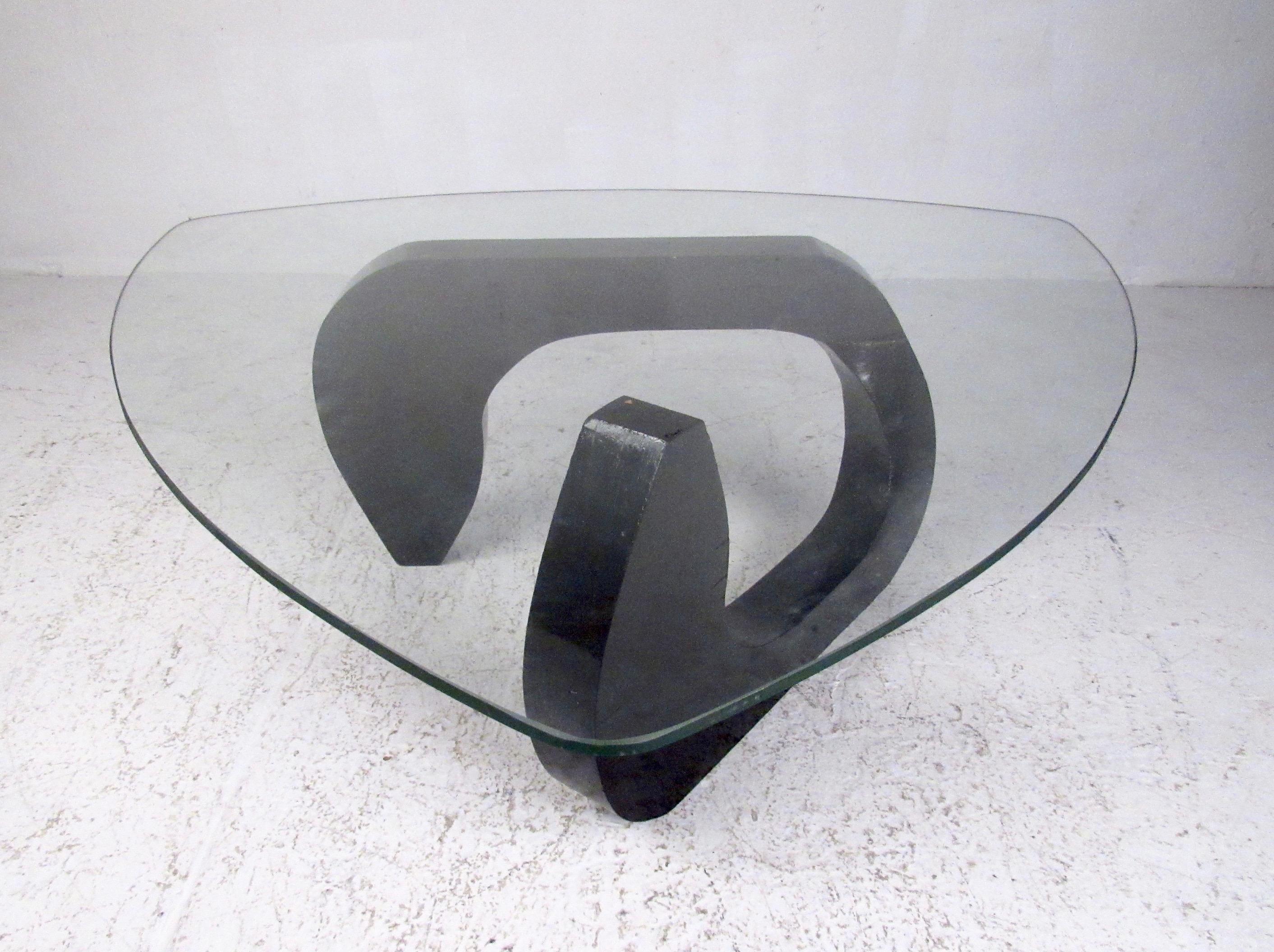 Vintage modern coffee table features shapely wood base topped with triangular glass top makes a simple yet elegant centrepiece to home or business seating arrangement. The Noguchi style of the piece adds a timeless midcentury style addition in any