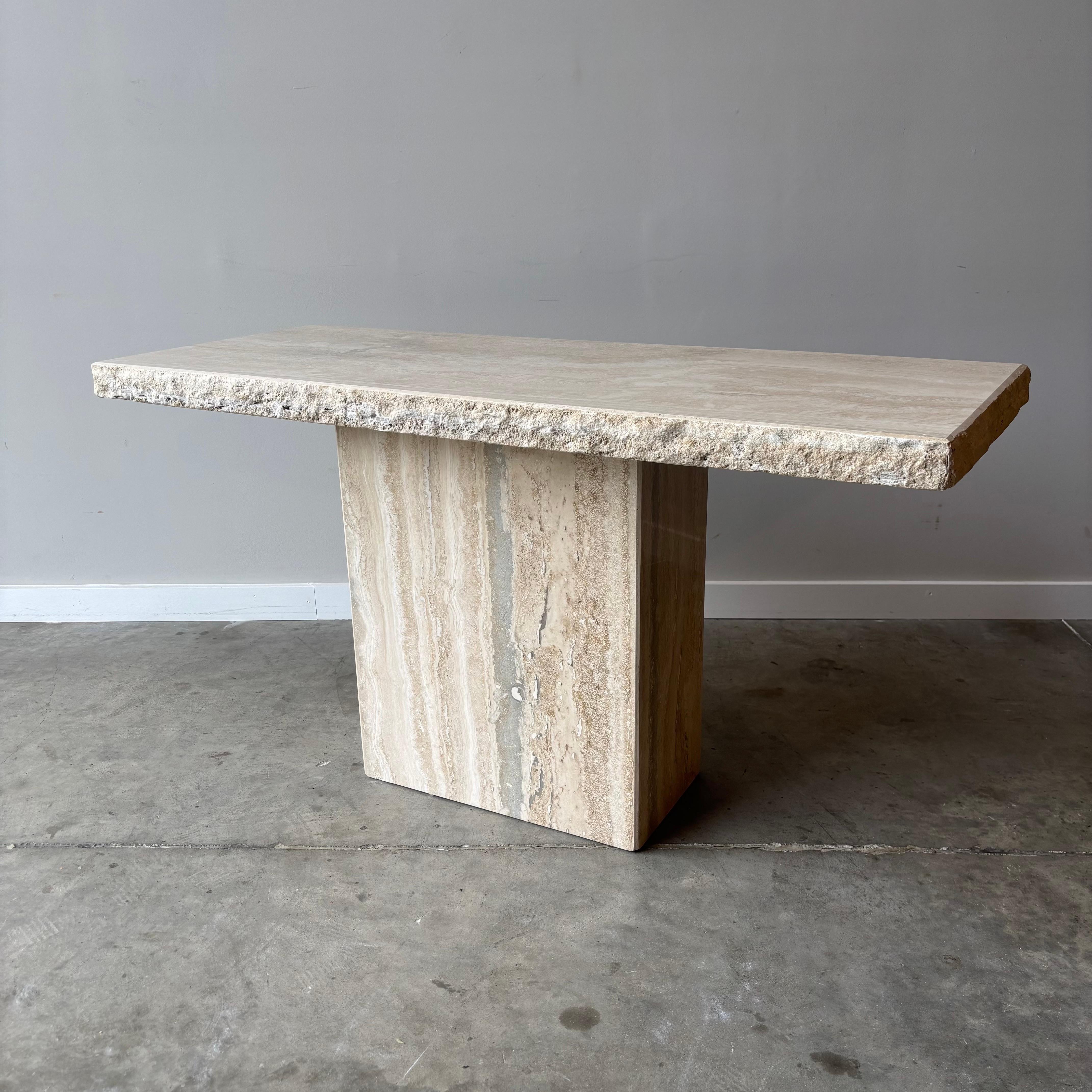 Esta mesa de travertino con borde de cantera tiene un aire minimalista dada la sencillez del material. El tablero expuesto de la mesa y la base son lisos. El tablero de la mesa tiene un borde de cantera, que combina maravillosamente las dos