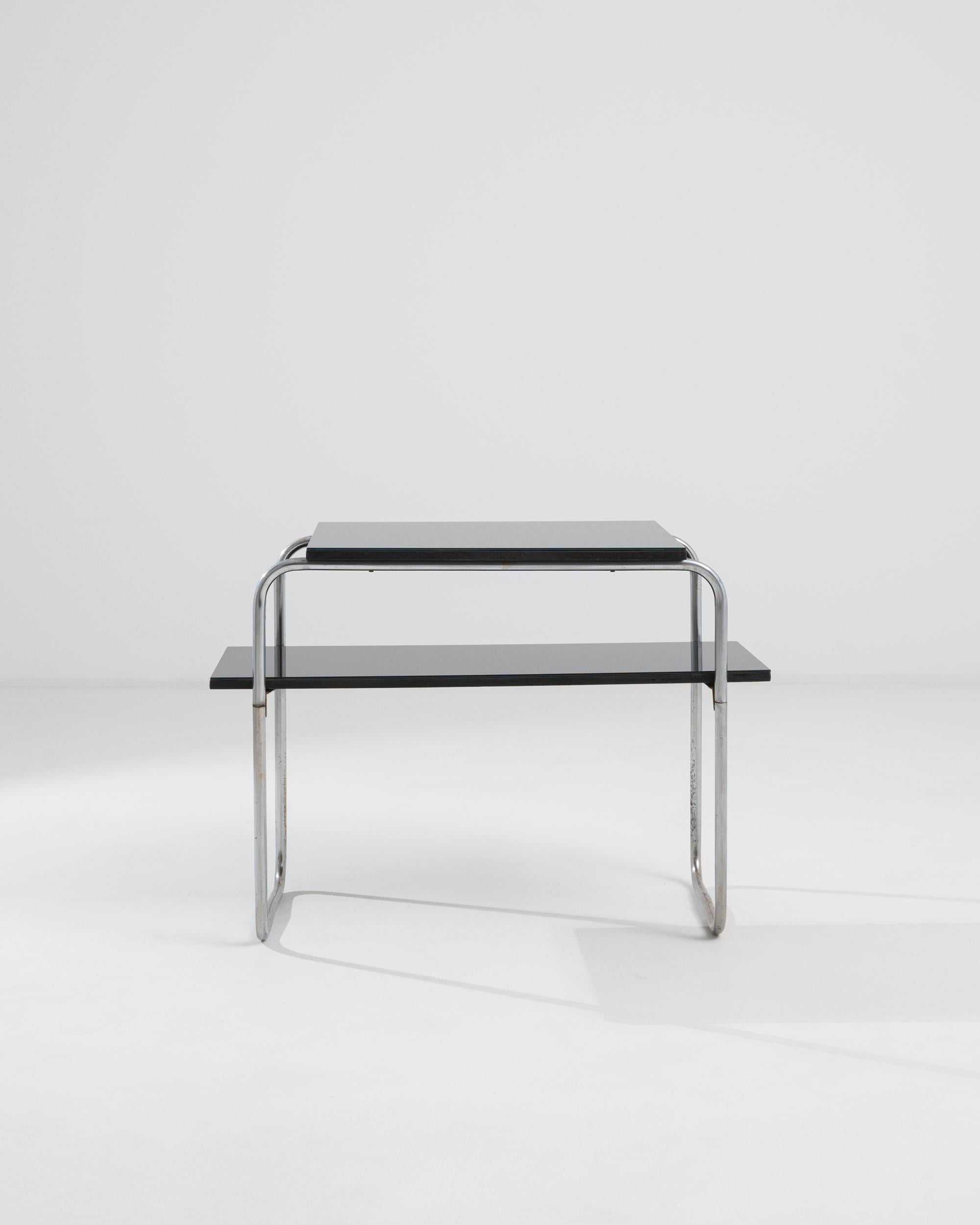 A side table made from wood, glass and metal from 20th century Czechia. This side table is composed of a simple, yet satisfying construction. Hollow metal twists this way and then that to two support its two gleaming shelves. Its materials and