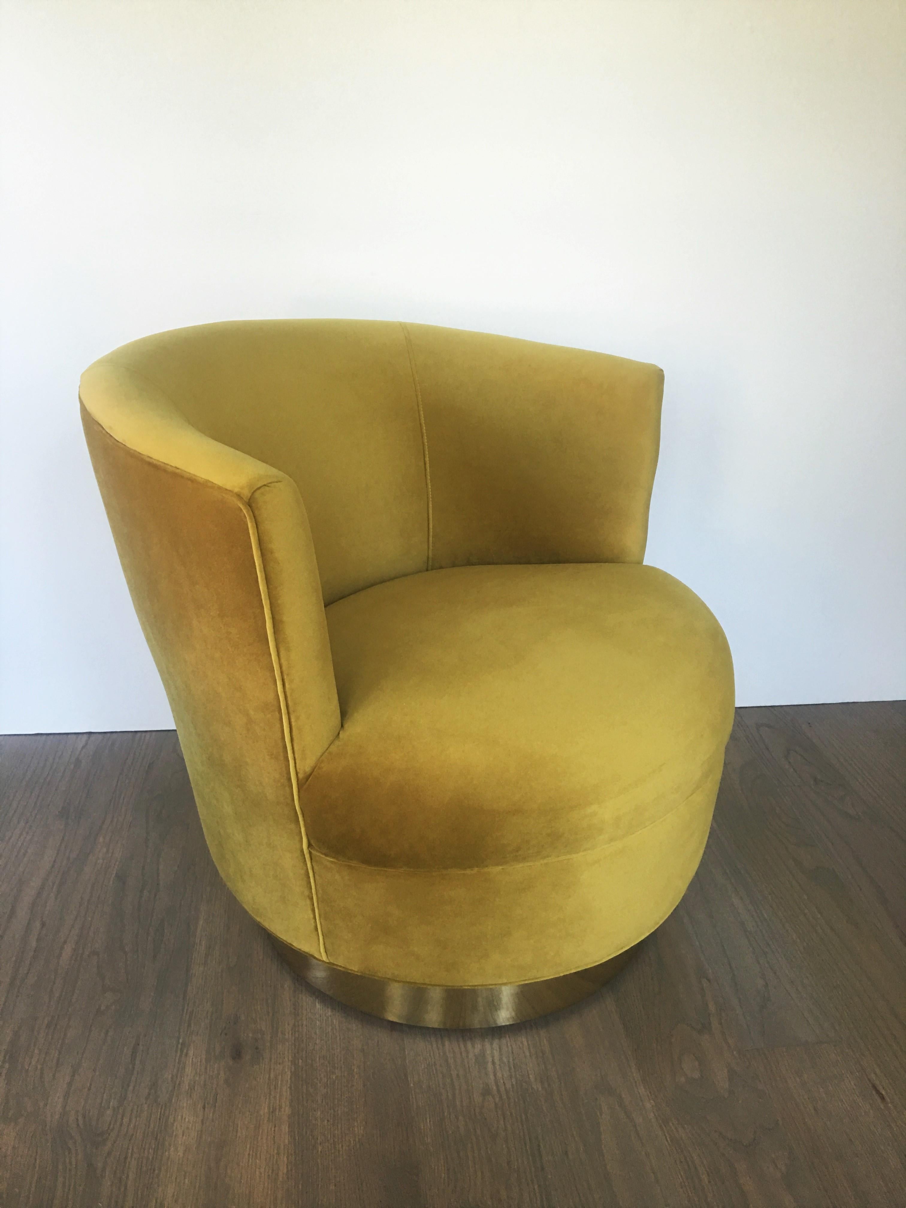 Stunning pair of swivel lounge chairs, recently recovered in a gold colored velvet. Features clean modern lines, barrel backs with the uppers raised on swivelling brass trimmed plinths.

  