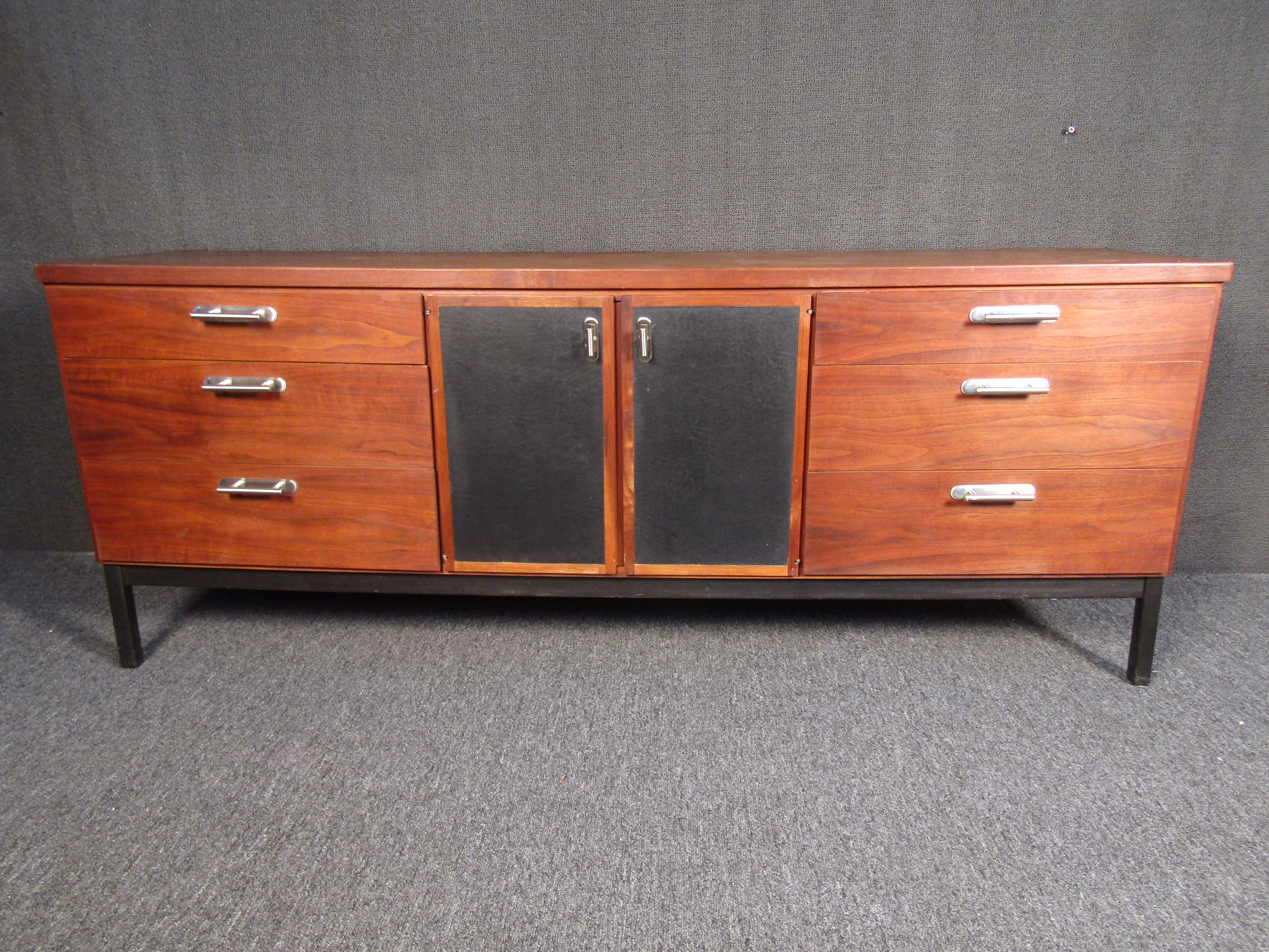 Vintage credenza that combines walnut woodgrain with chrome accents for a stunning Mid-Century Modern look. Plenty of storage is offered between six drawers on either side and an additional three drawers inside the middle compartment. Black paneled