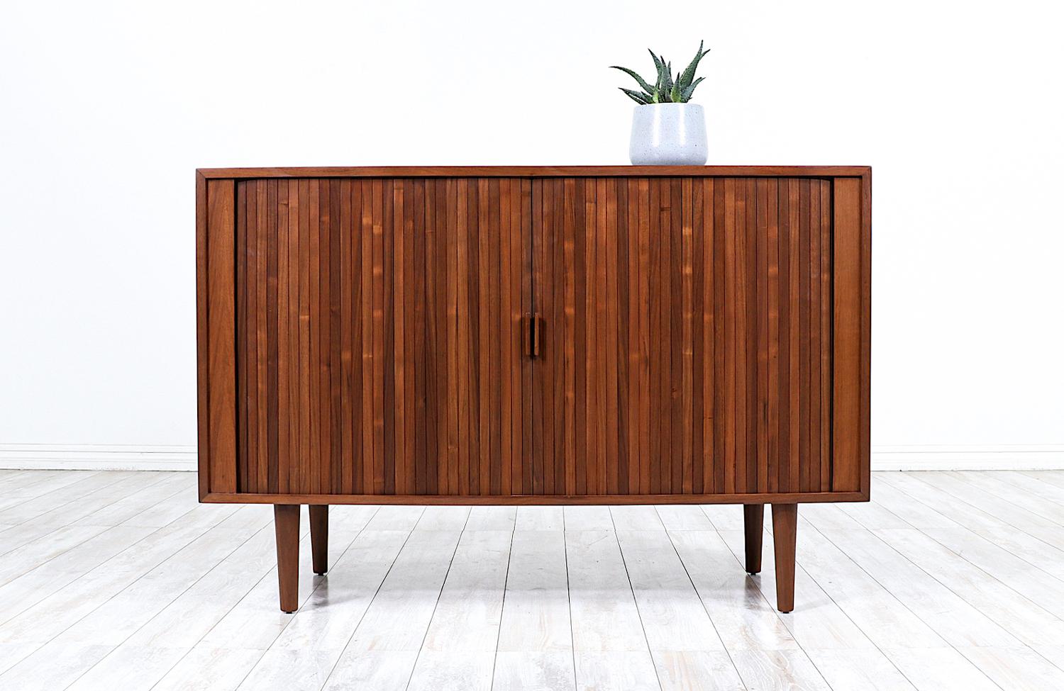 Mid-Century Modern tambour door credenza designed and manufactured in the United States circa 1960’s. Low in profile and compact in size, this beautifully refinished walnut storage unit is accented with inconspicuous door pulls for functional ease.