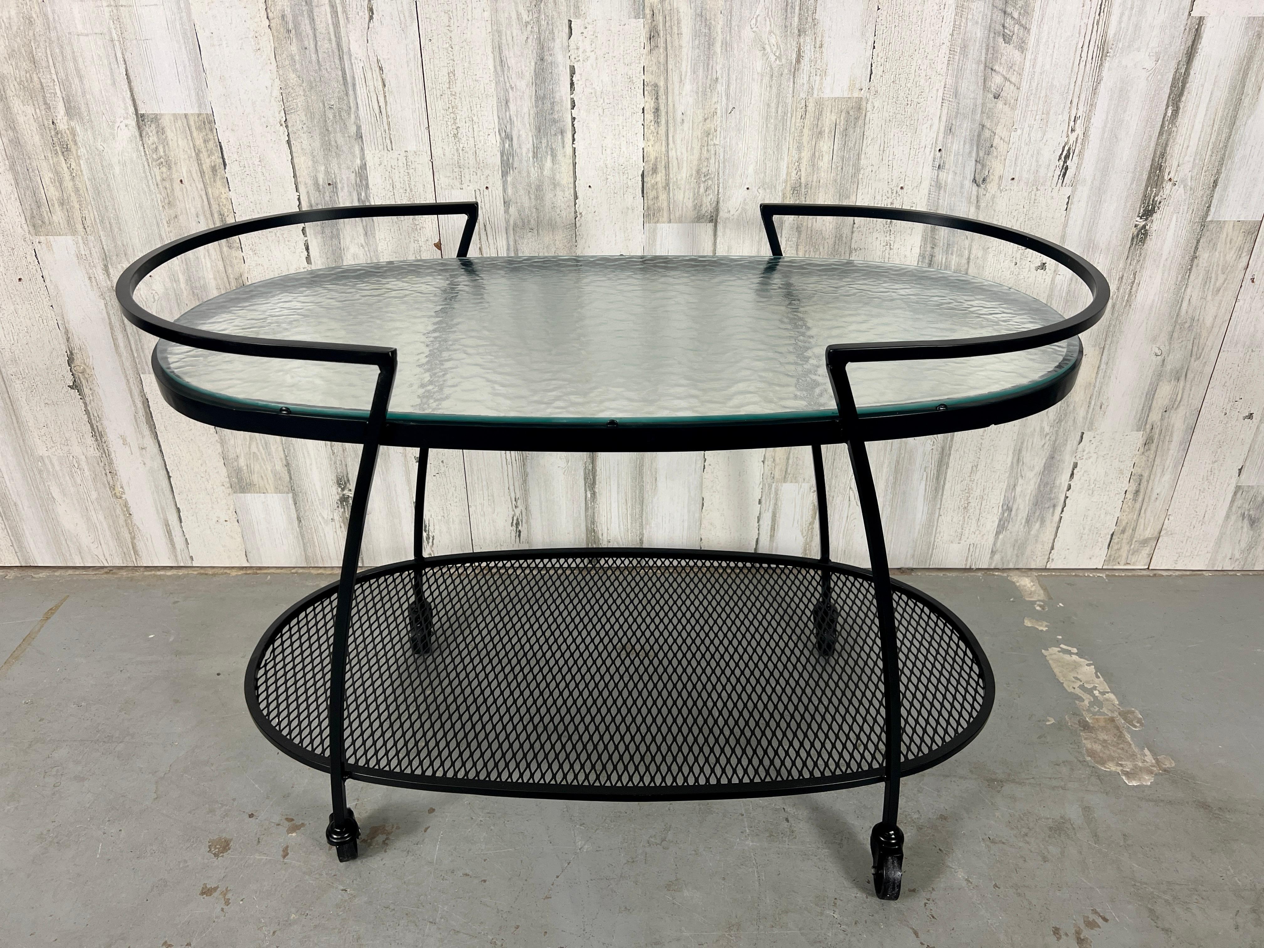 Modernist iron bar cart made by Woodard patio furniture company. Maintains it's original pebble glass with new powder coat coated metal. A beautiful addition to any patio or poolside venue. 