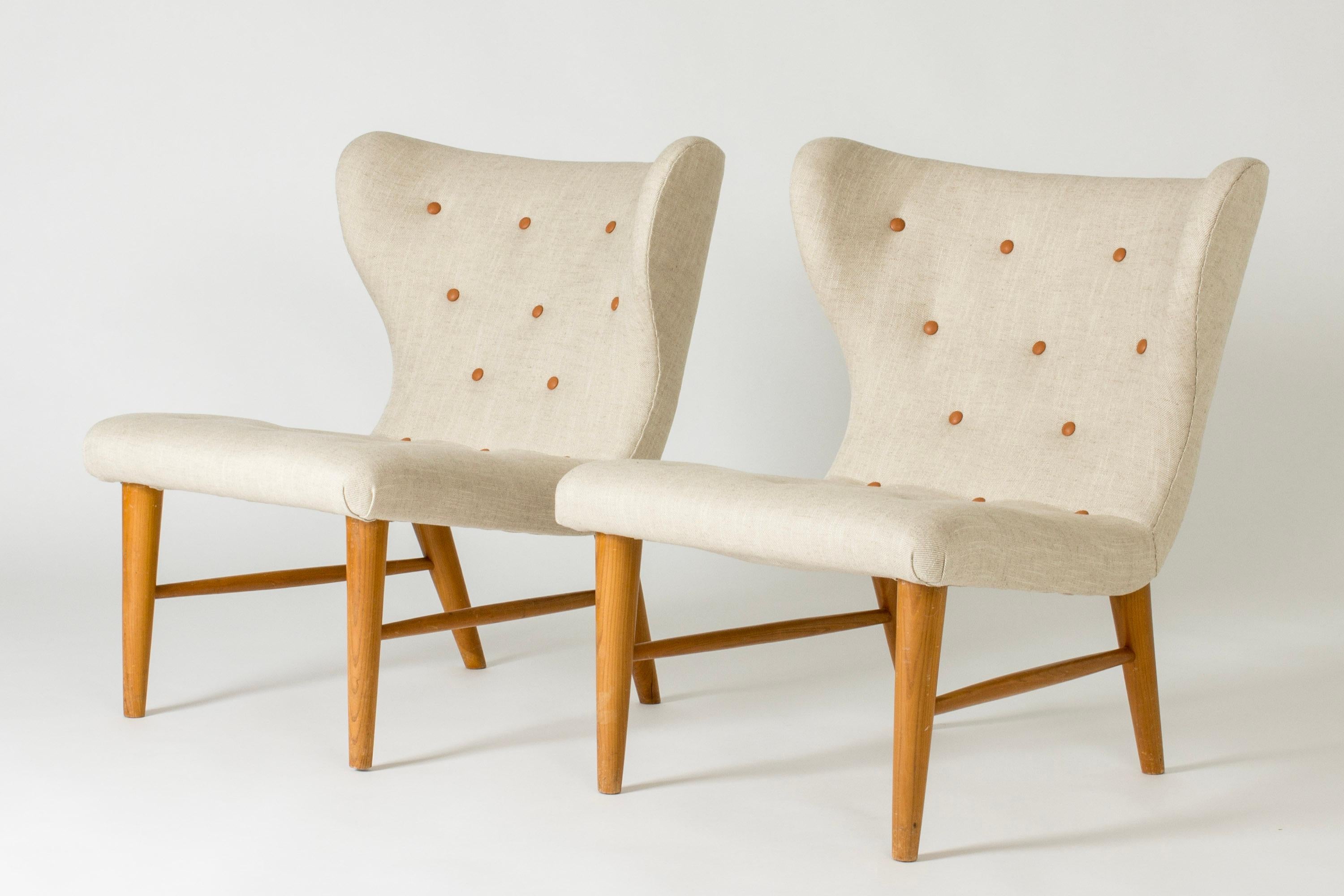 Pair of rare lounge chairs by Eric Karlén with bold lines. Upholstered with linen and elegant leather dressed buttons. Beech legs.