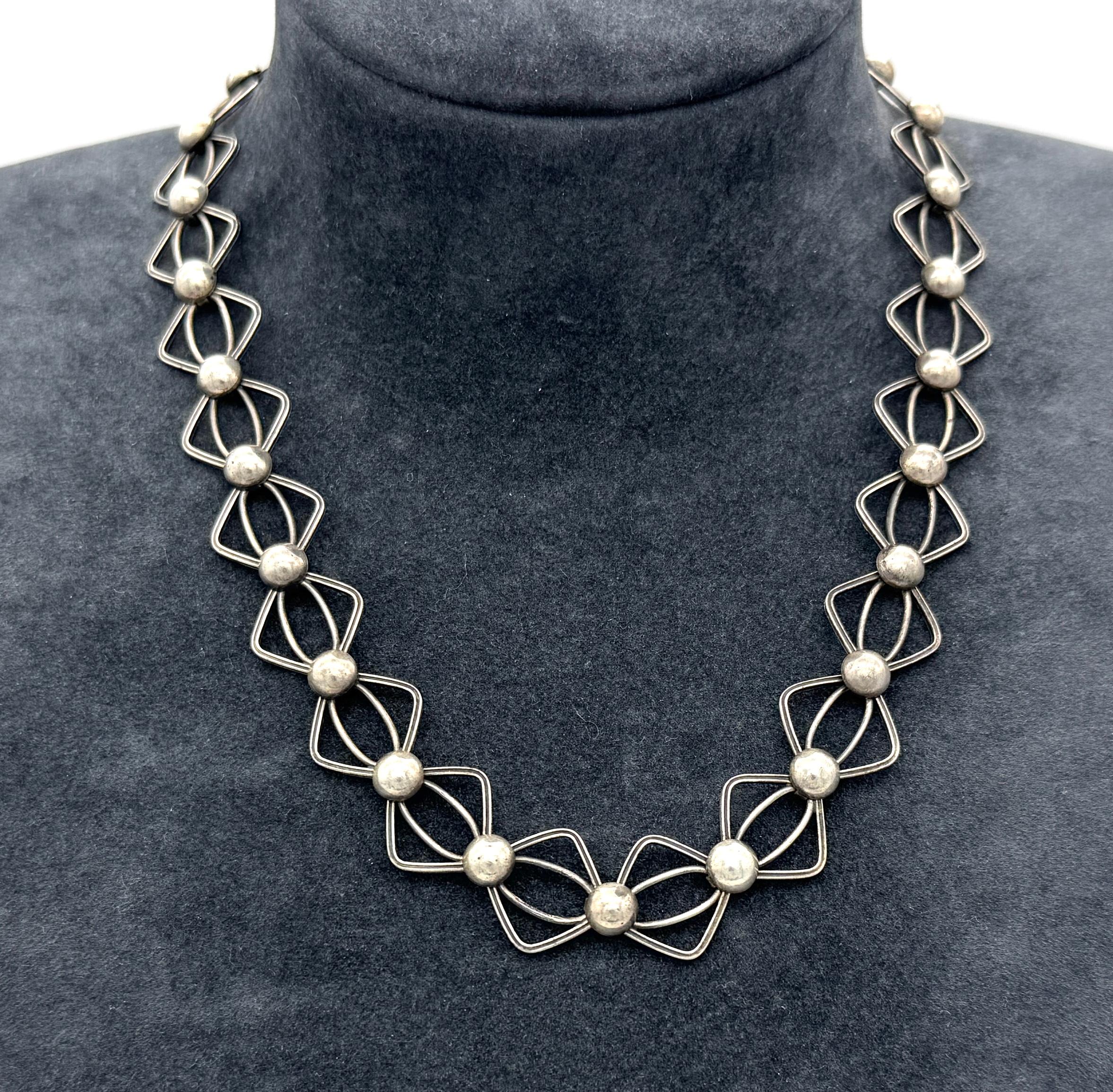 This vintage modernist necklace was handcrafted in 1925 ca. The necklace is made up from grooved square frames with rounded corners. Each corner has an oval link in its center. The squares are joined by links decorated with half balls. The necklace