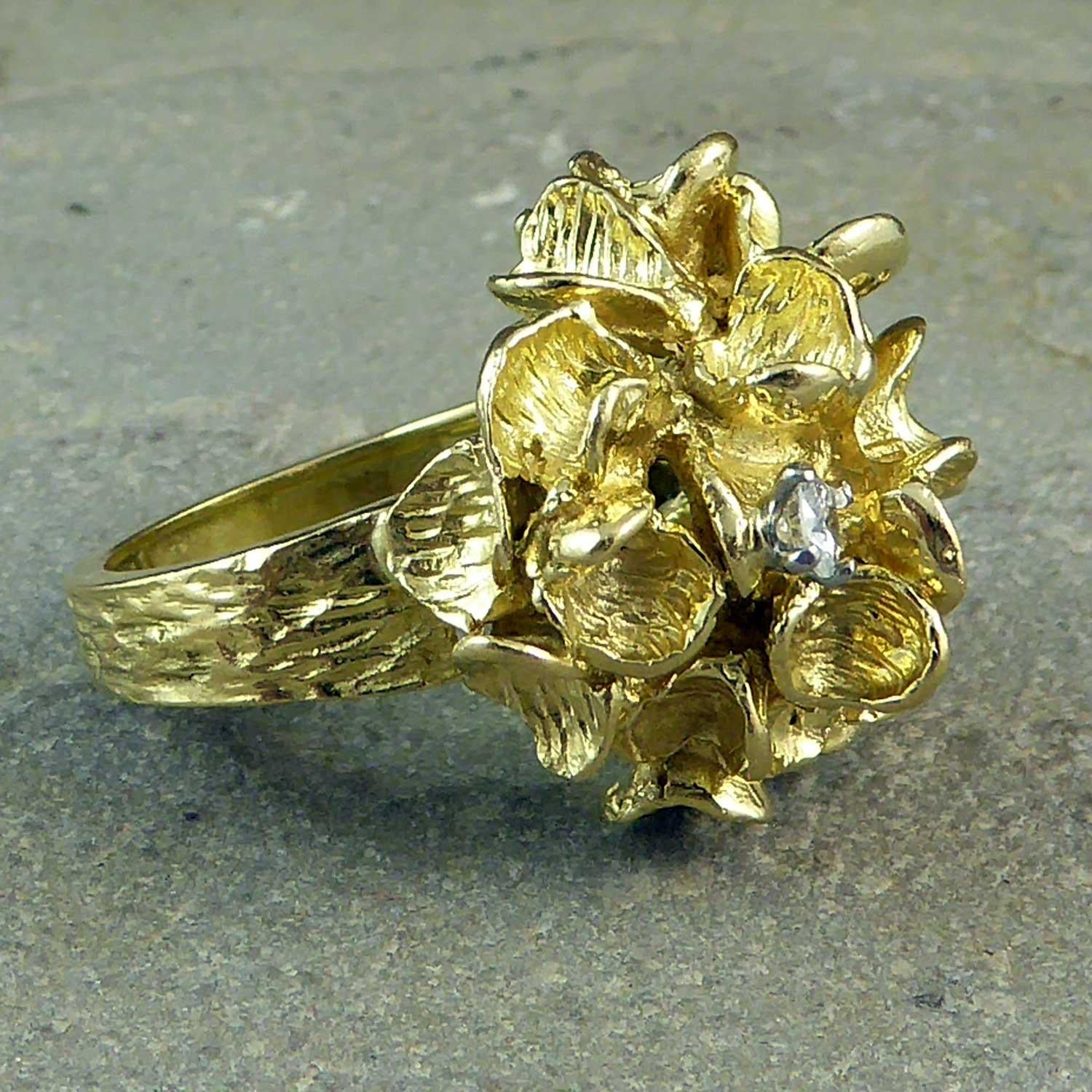 A fabulous vintage right hand ring from the 1960s in the form of a flower head cluster, possibly at stylized hydrangea?  The cluster of petals have a semi-matte finish one of which sports a brilliant cut diamond approx. 3.0mm diameter.  The head of