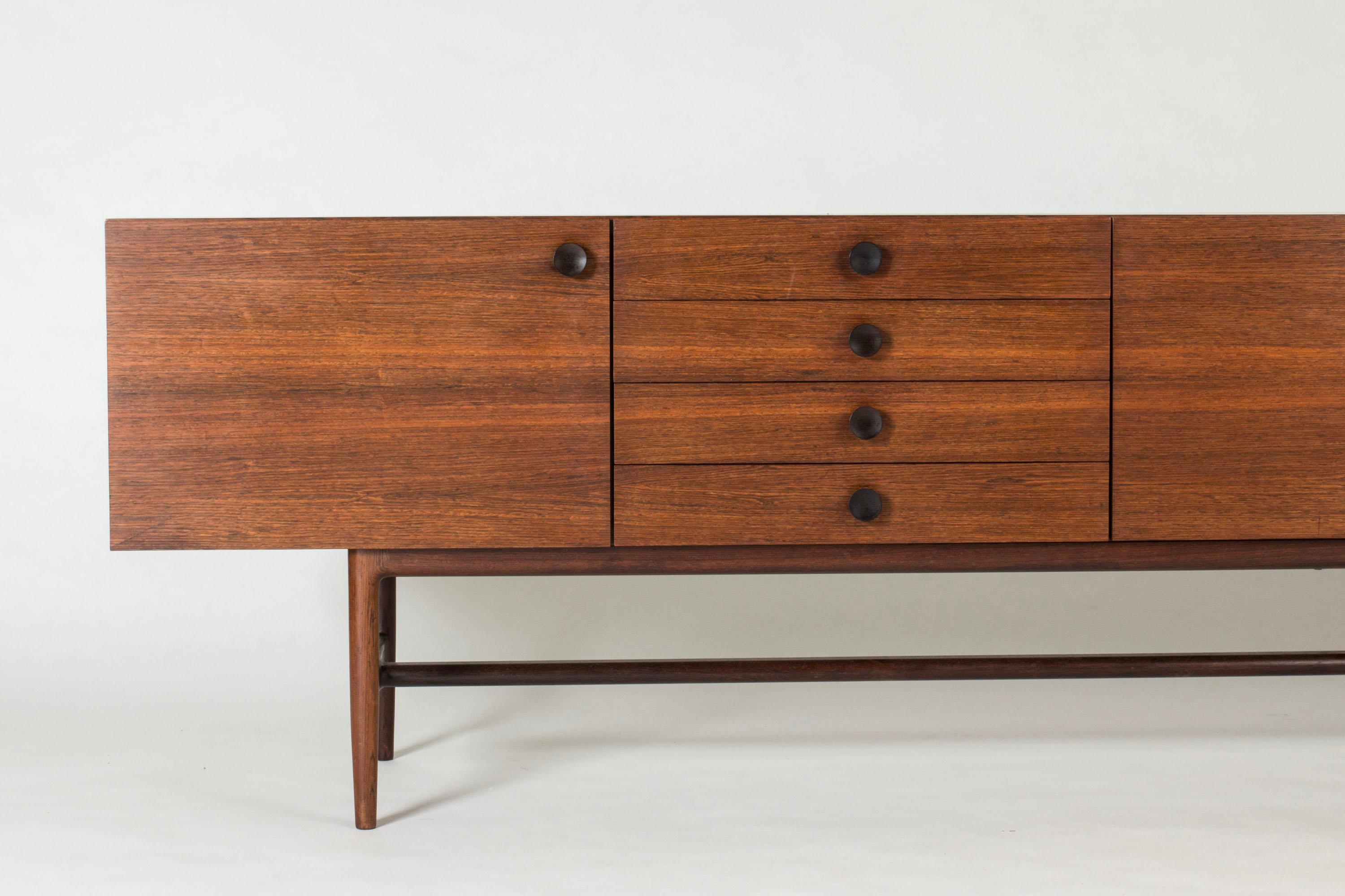 Cool, rare sideboard by Ib Kofod Larsen, made from rosewood. Clean design with a smooth veneer pattern. Cabinet doors and drawers with decorative round wooden handles in a darker nuance. Back also dressed with veneer.