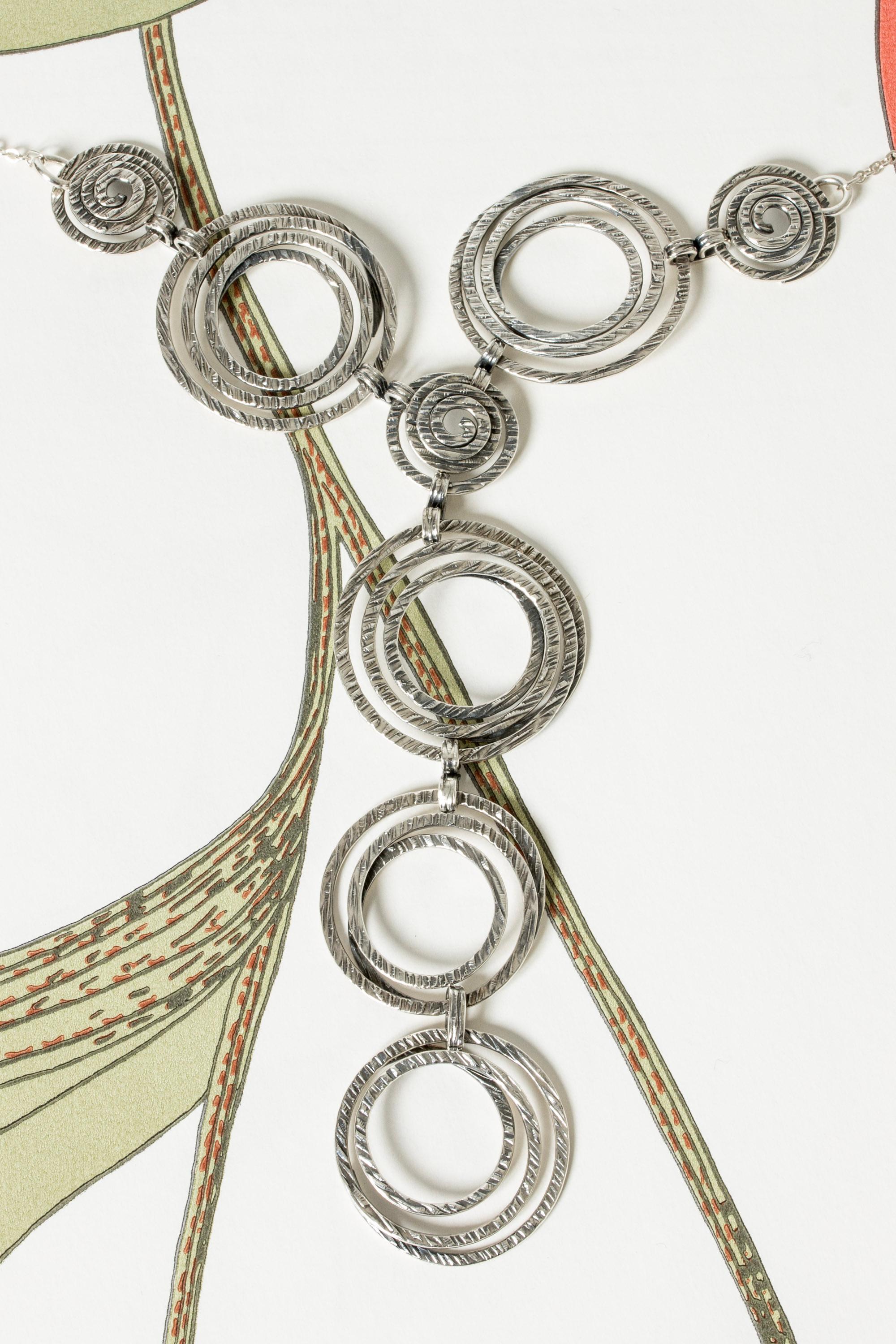 Striking modernist silver collier by Elis Kauppi, with a large pendant of spirals. Rugged surface on the spirals, a subtle folkloristic feel. Looks amazing with a plunging neckline.

Length of chain 34 cm, length of pendant 19 cm.
