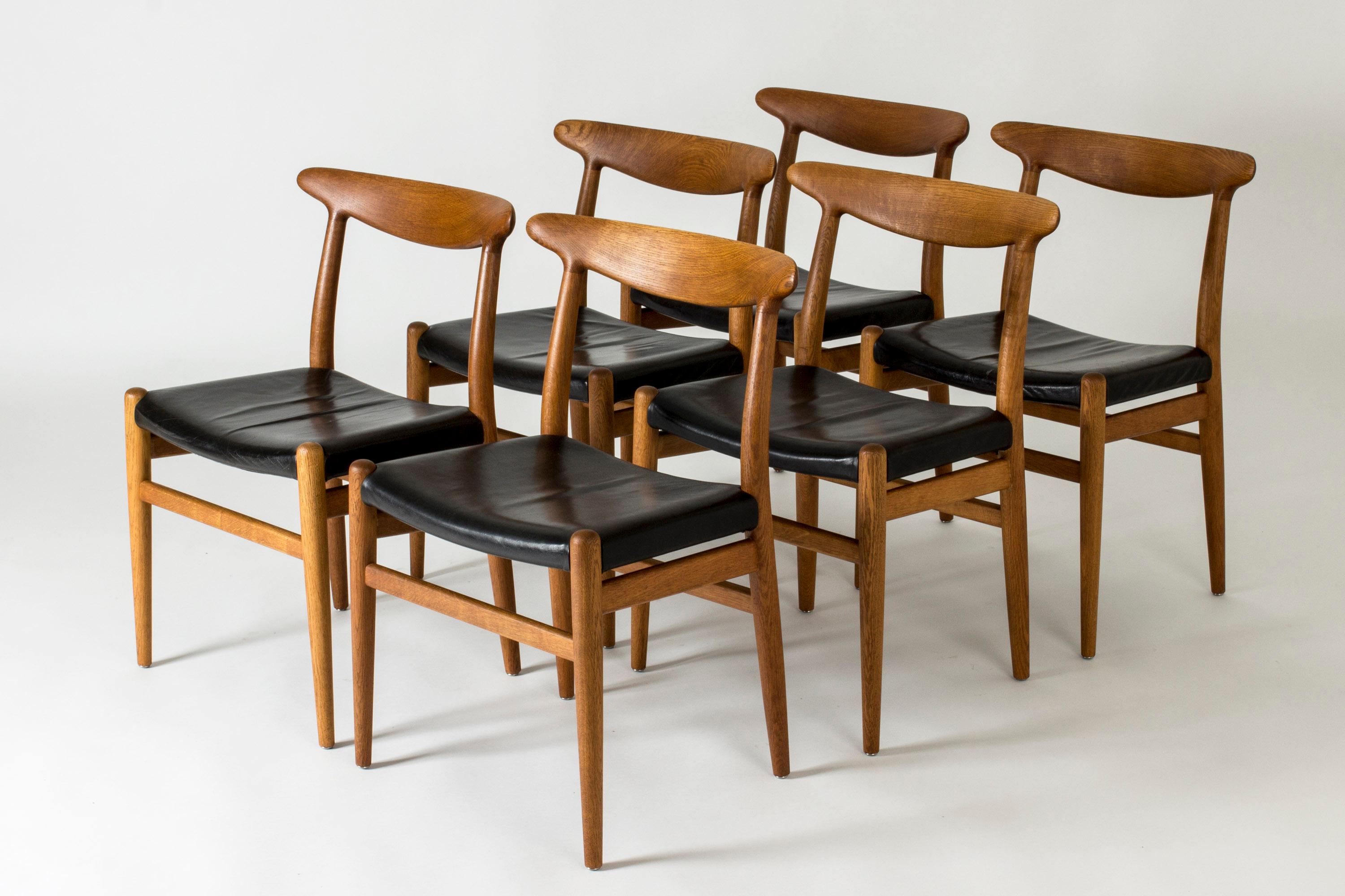 Set of six beautiful “W2” dining chairs by Hans J. Wegner, made from oak with black leather seats. Great woodgrain that follows the lines of the seamlessly sculpted backrests.