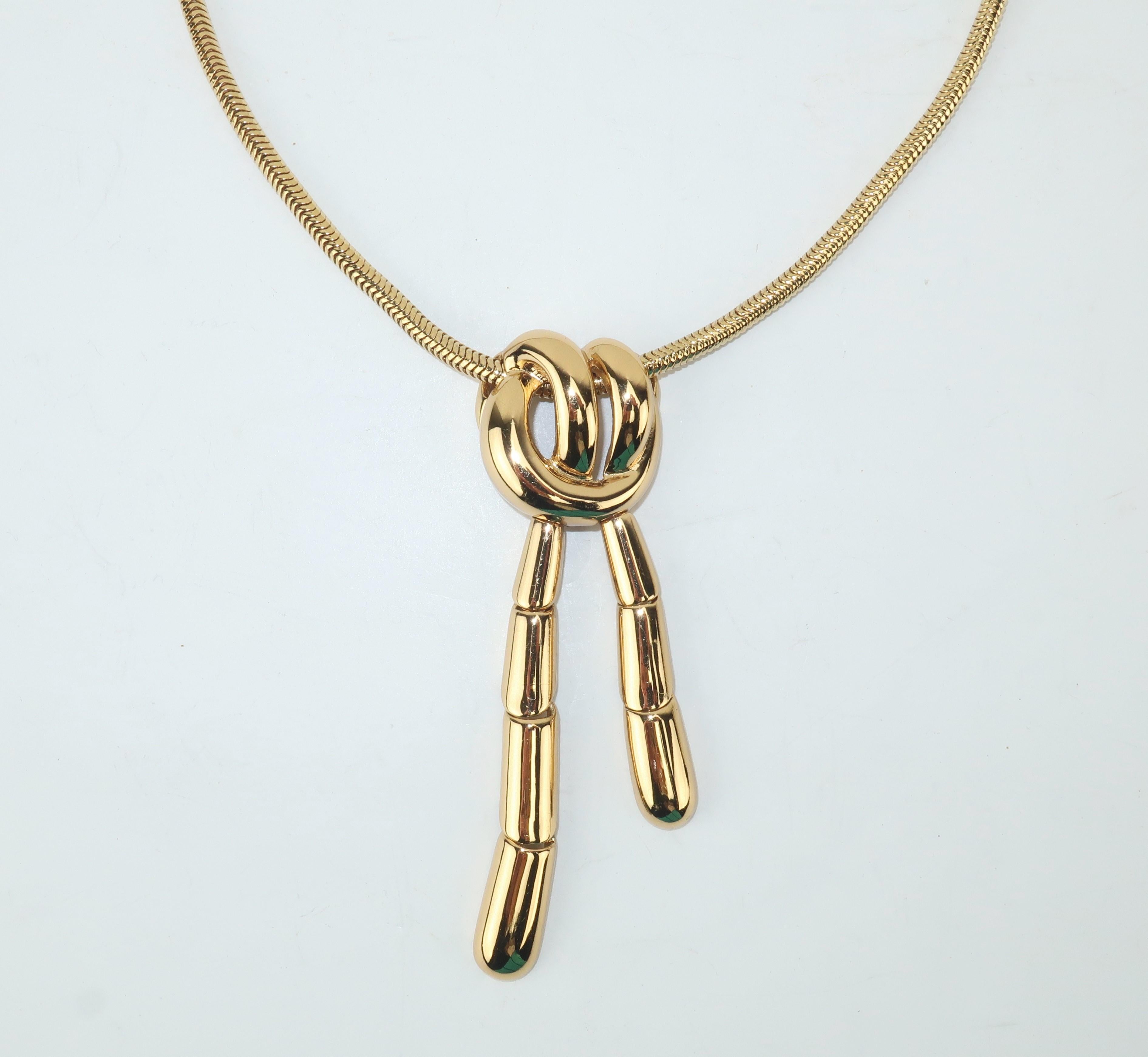 A close fitting Monet gold tone pendant necklace featuring a faux knot created from articulated segments.  The knot is suspended from a serpentine chain outfitted with a clamp closure and the design offers a unique fluidity that is subtly