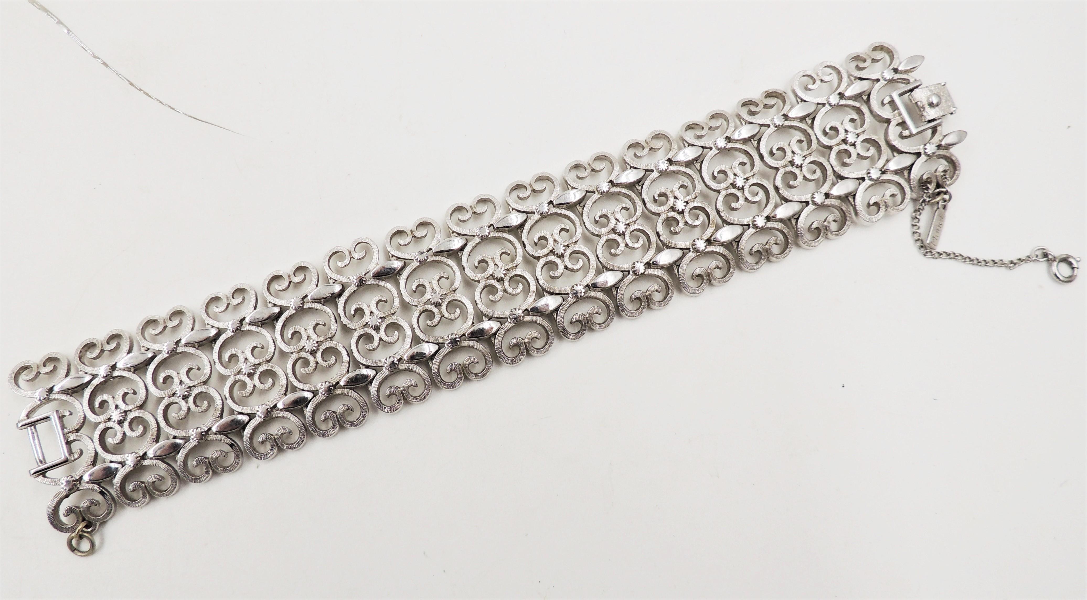 Rhodium plated filigree open work bracelet with fold over clasp and security chain. Marked 