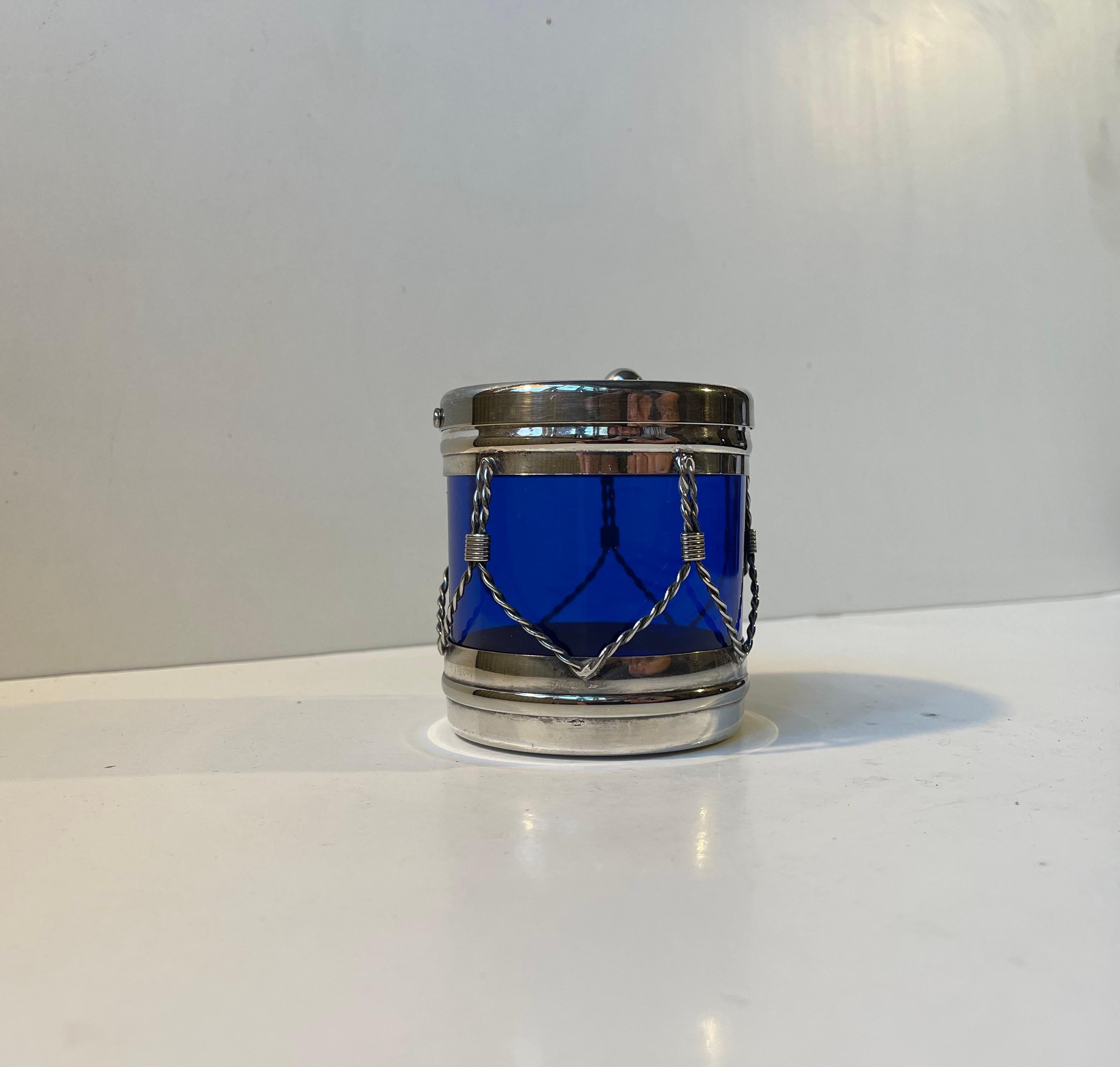Piccolo salvadanaio decorativo a forma di tamburo. È realizzato in metallo placcato argento e vetro blu cobalto. Puoi accedere al suo contenuto girando il coperchio. Prodotto da Vieners International a Hong Kong per il rivenditore Mema in Svezia,